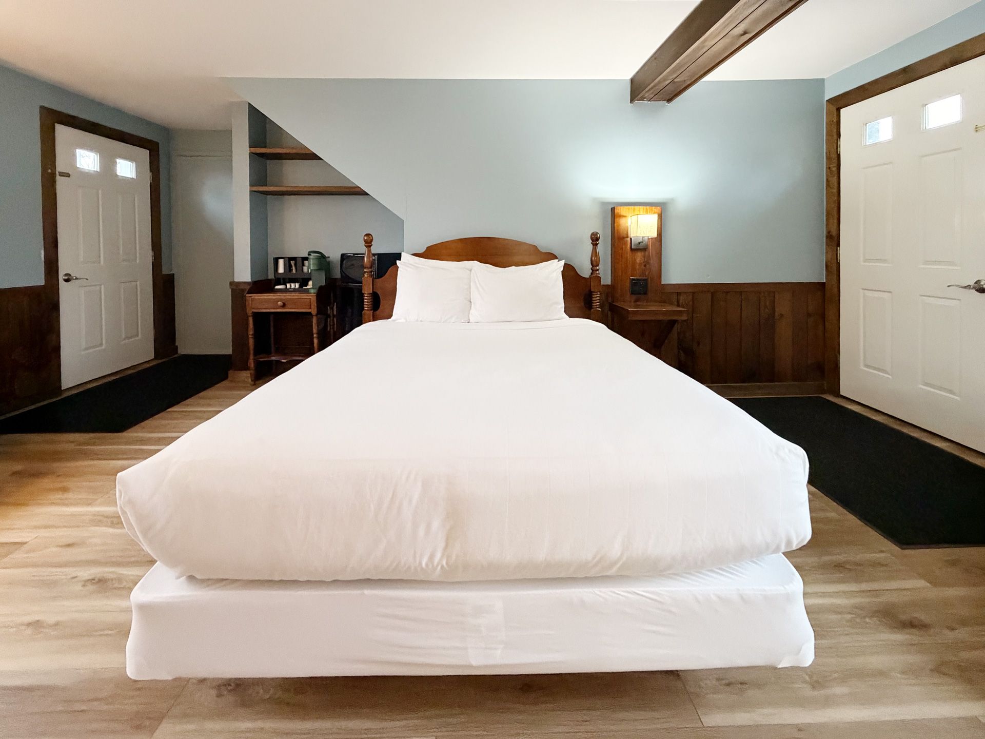 Bright bedroom with a white bed centered between two doors and wood-paneled walls.