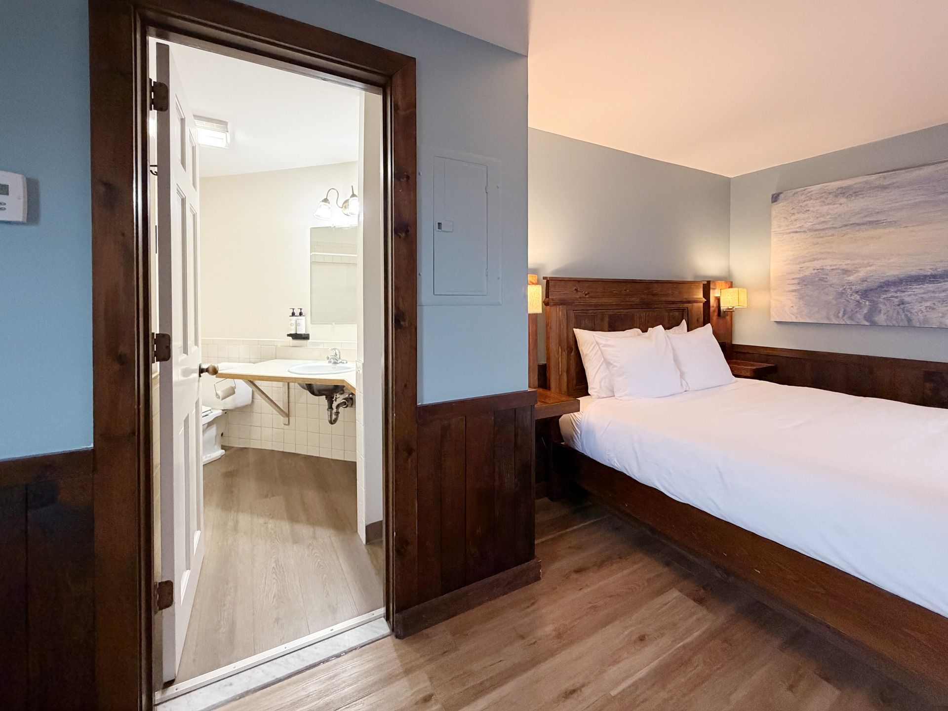Hotel room with wooden bed, open bathroom door, and hardwood floor