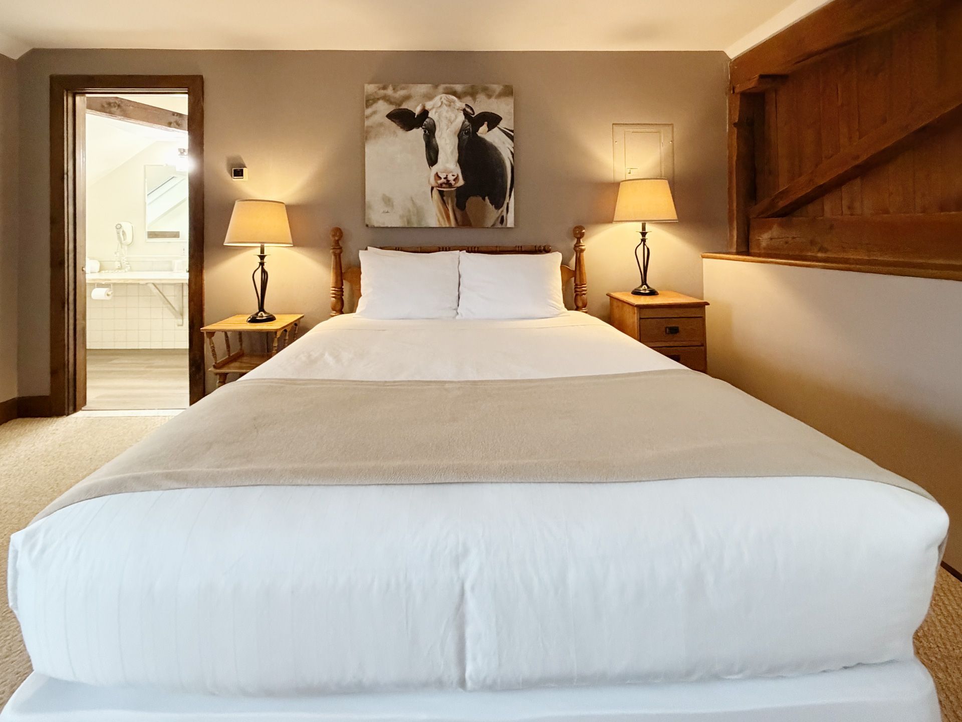 Cozy bedroom with a neatly made bed, nightstands, lamps, and an open doorway to a bathroom