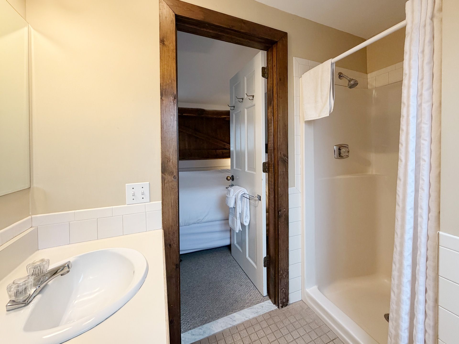 Bathroom with sink, mirror, and tub-shower stall beside an open doorway to a carpeted bedroom.