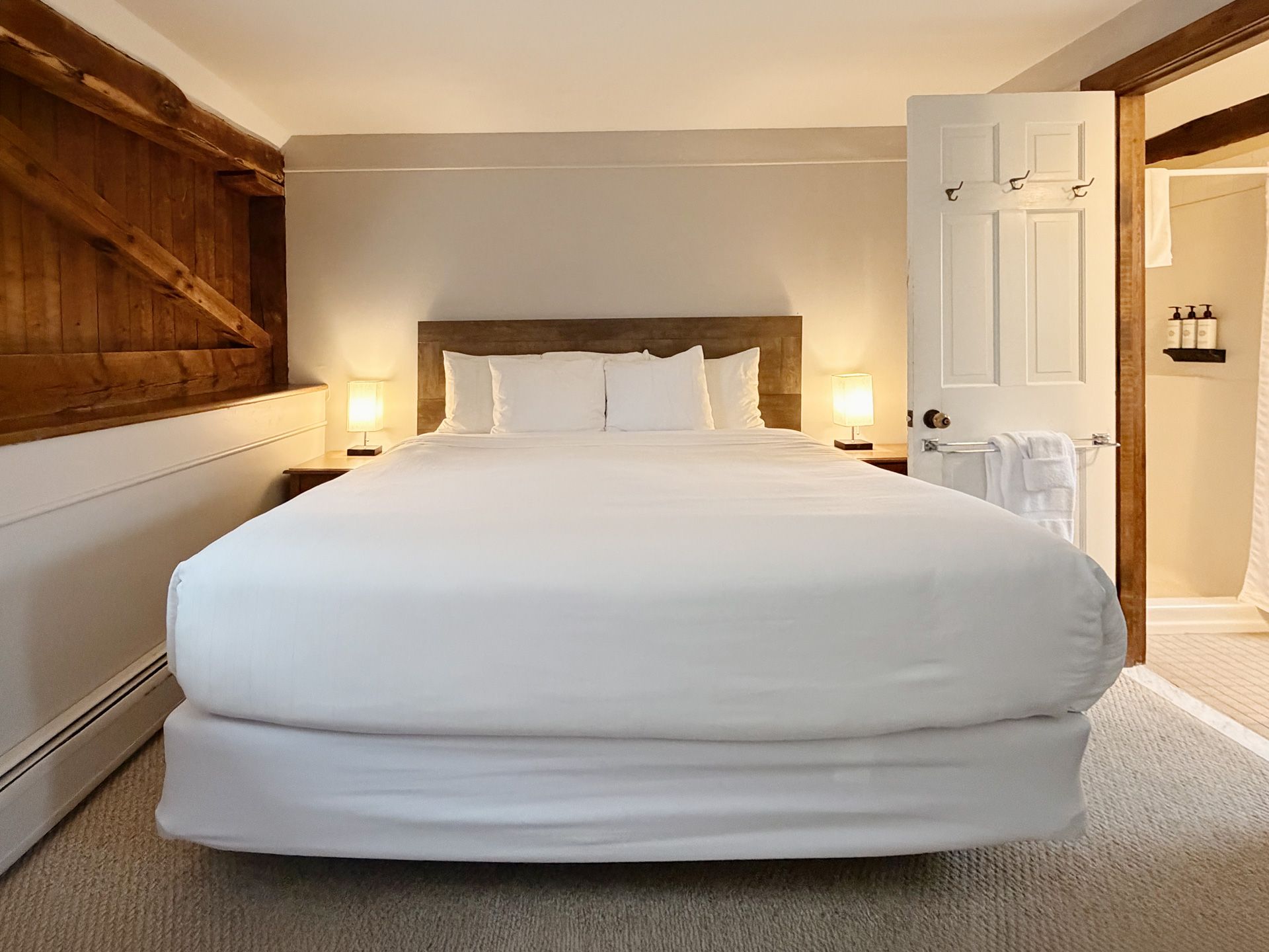 Cozy bedroom with a white bed, wooden shelving, bedside lamps, and an open door to the bathroom.