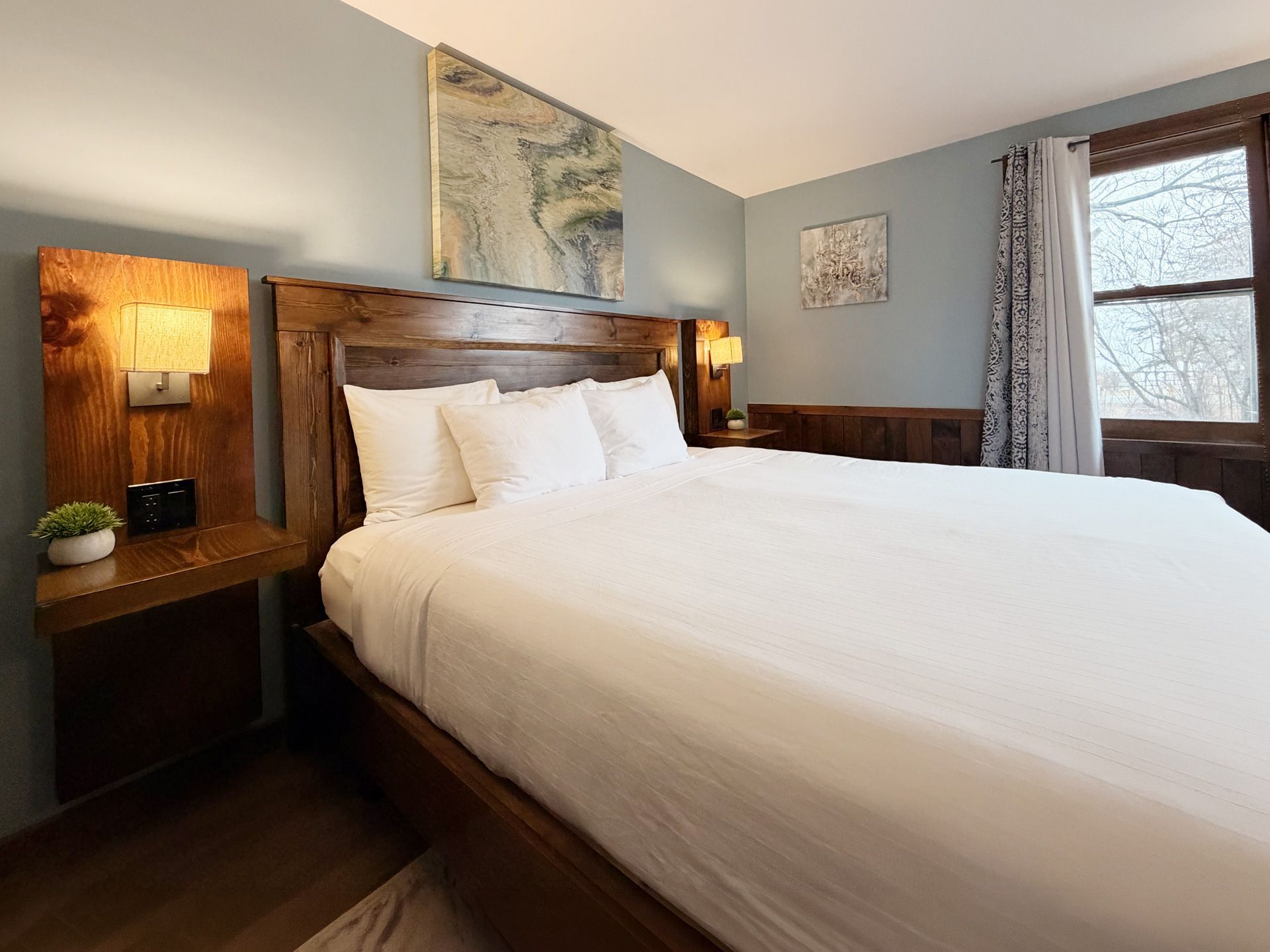 Cozy bedroom with a large bed, warm wood paneling, bedside lamps, and a window with curtains