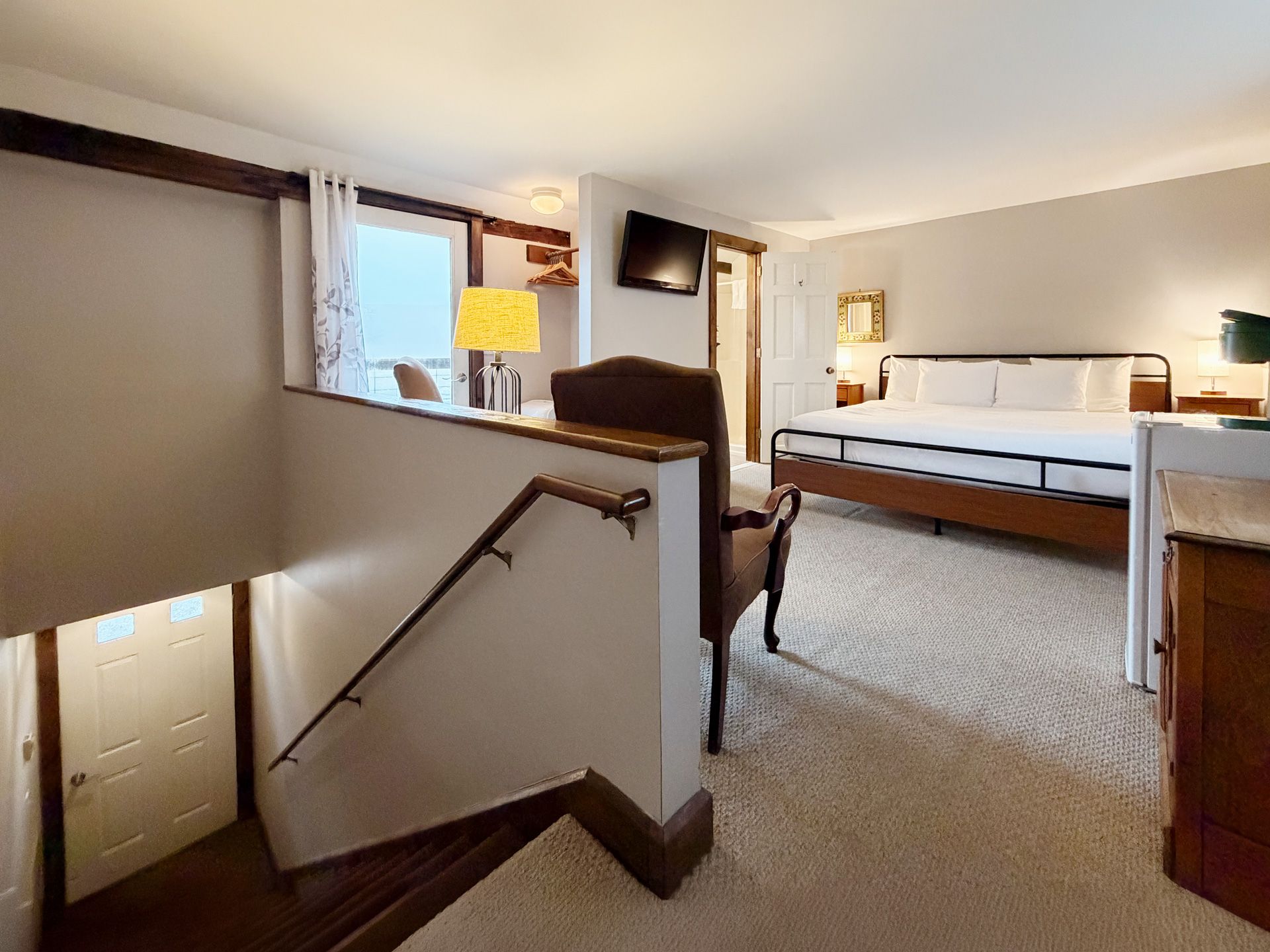 Hotel room with a staircase, bed, TV, and warm lighting