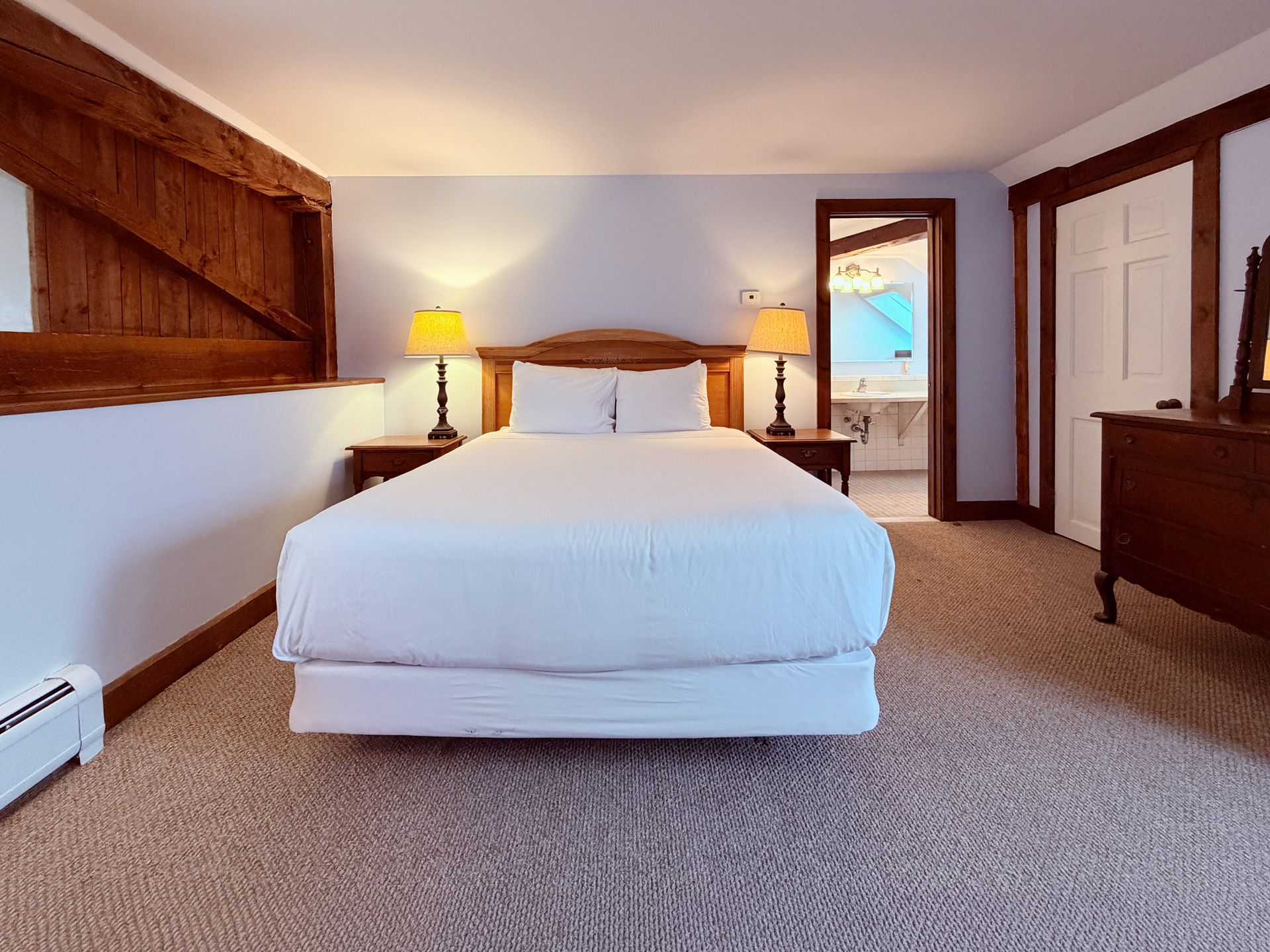 Cozy attic bedroom with a white bed, wooden beams, bedside lamps, and an open door to a balcony.