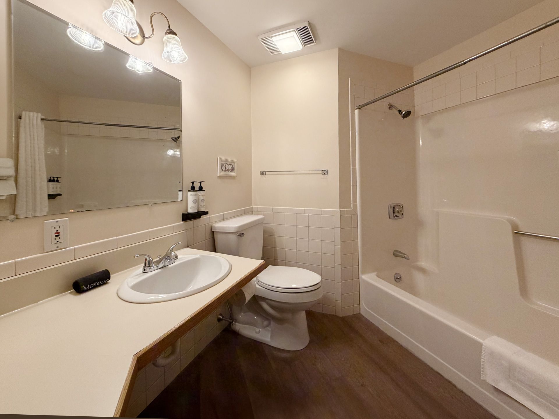 Beige bathroom with sink, mirror, toilet, tub, and wood-look floor.