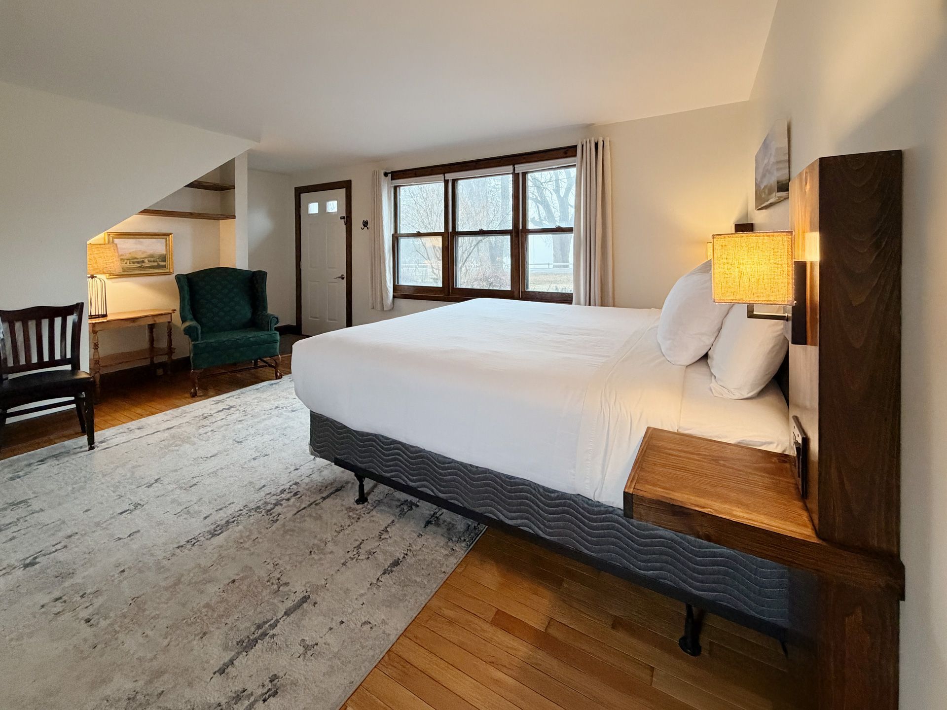 Bright bedroom with a large bed, windows, armchair, and warm lighting