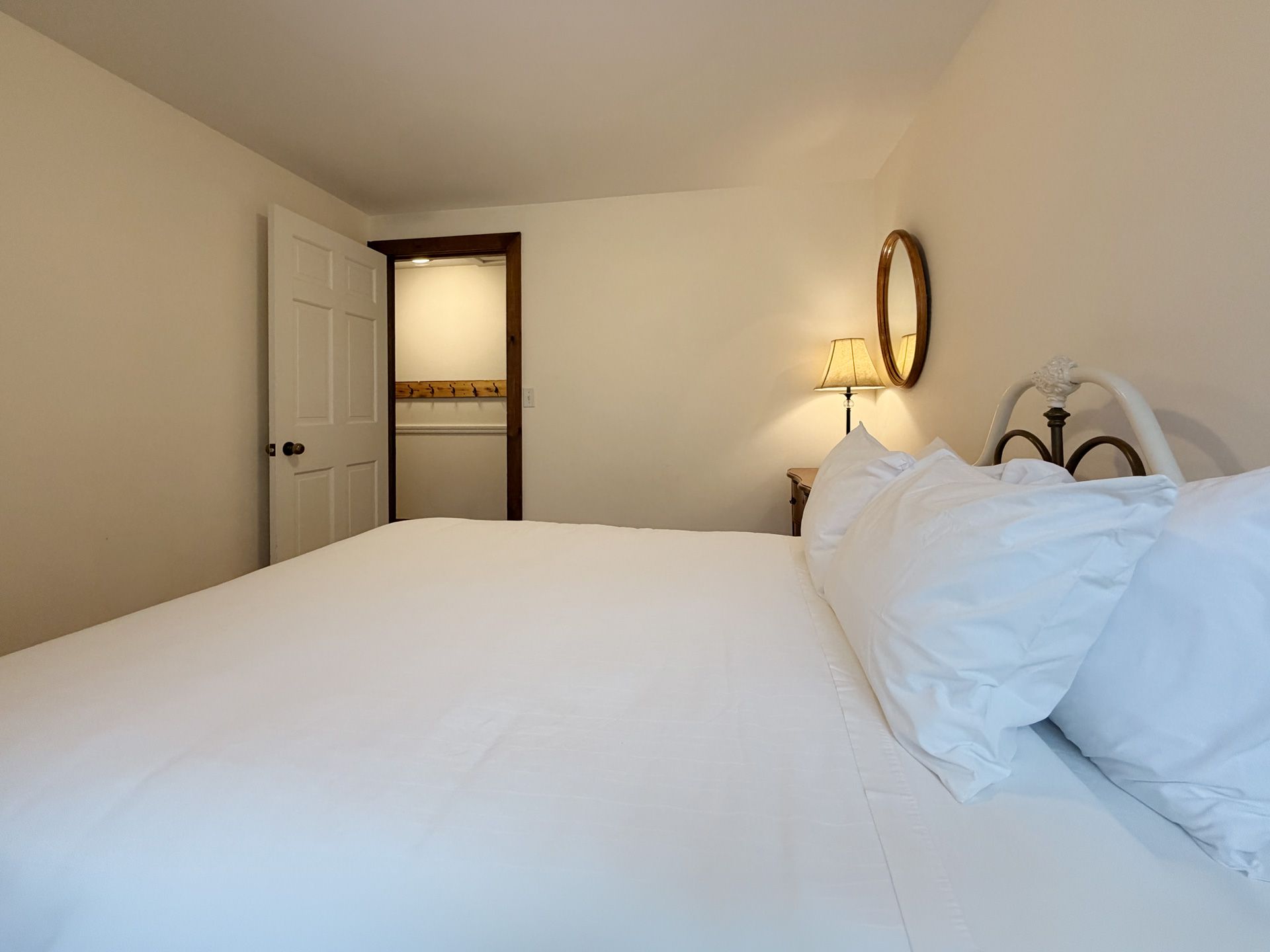Bright bedroom with a large white bed, open closet door, and a lit bedside lamp.