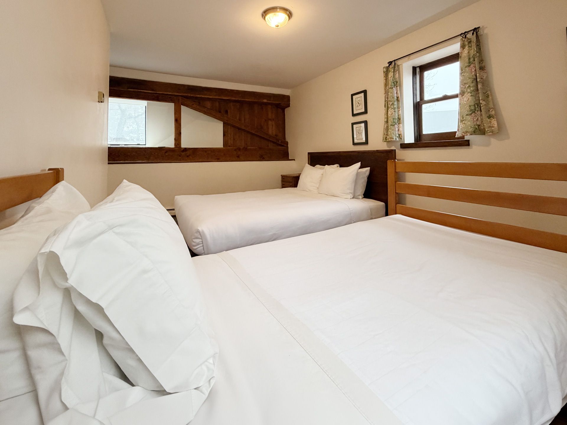 Small cozy bedroom with three white beds, wood accents, and a window with curtains