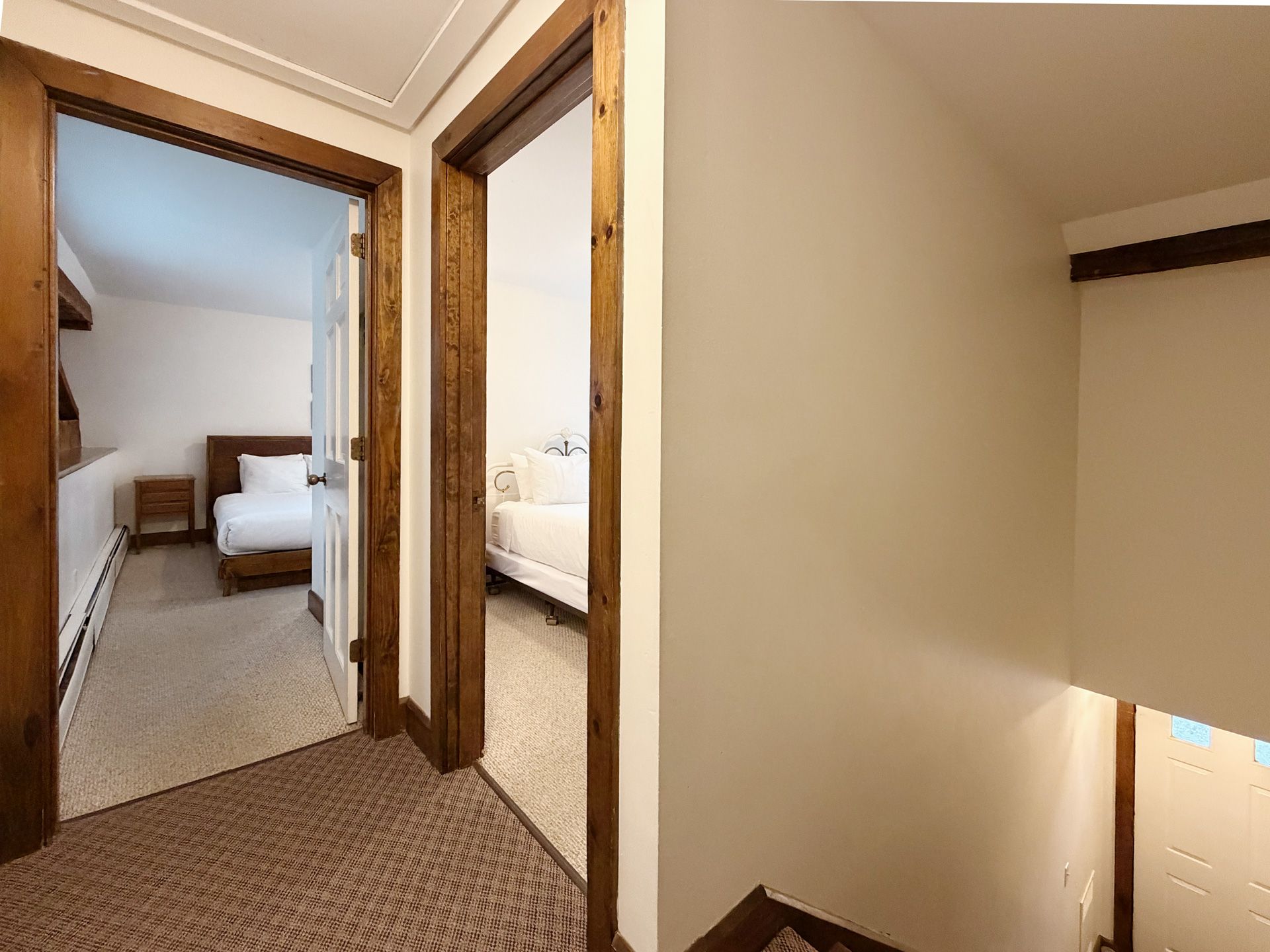 Hallway with two open bedroom doors and carpeted stairs, showing a bed in each room.