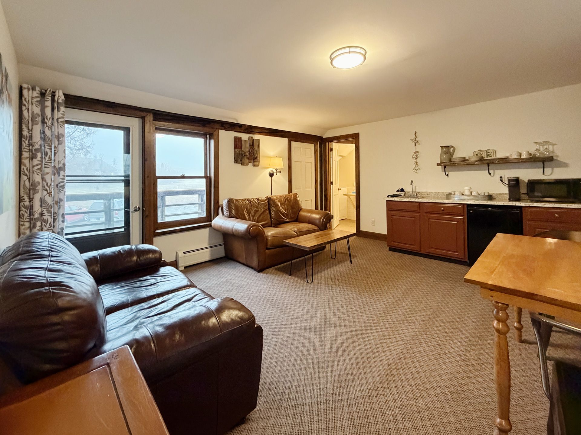 Living room with brown leather sofas, carpet, windows, and kitchen counter in the background