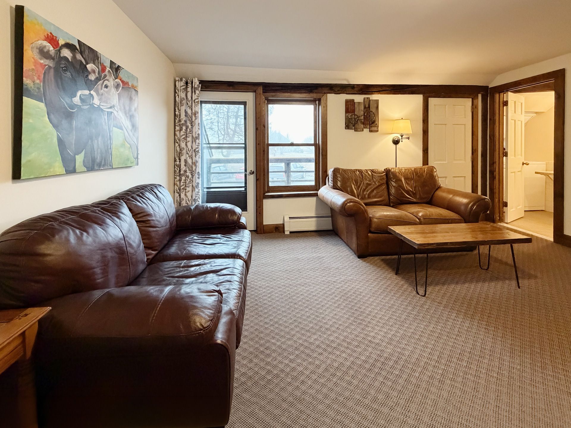Living room with brown leather sofas, coffee table, large window, and colorful wall art.