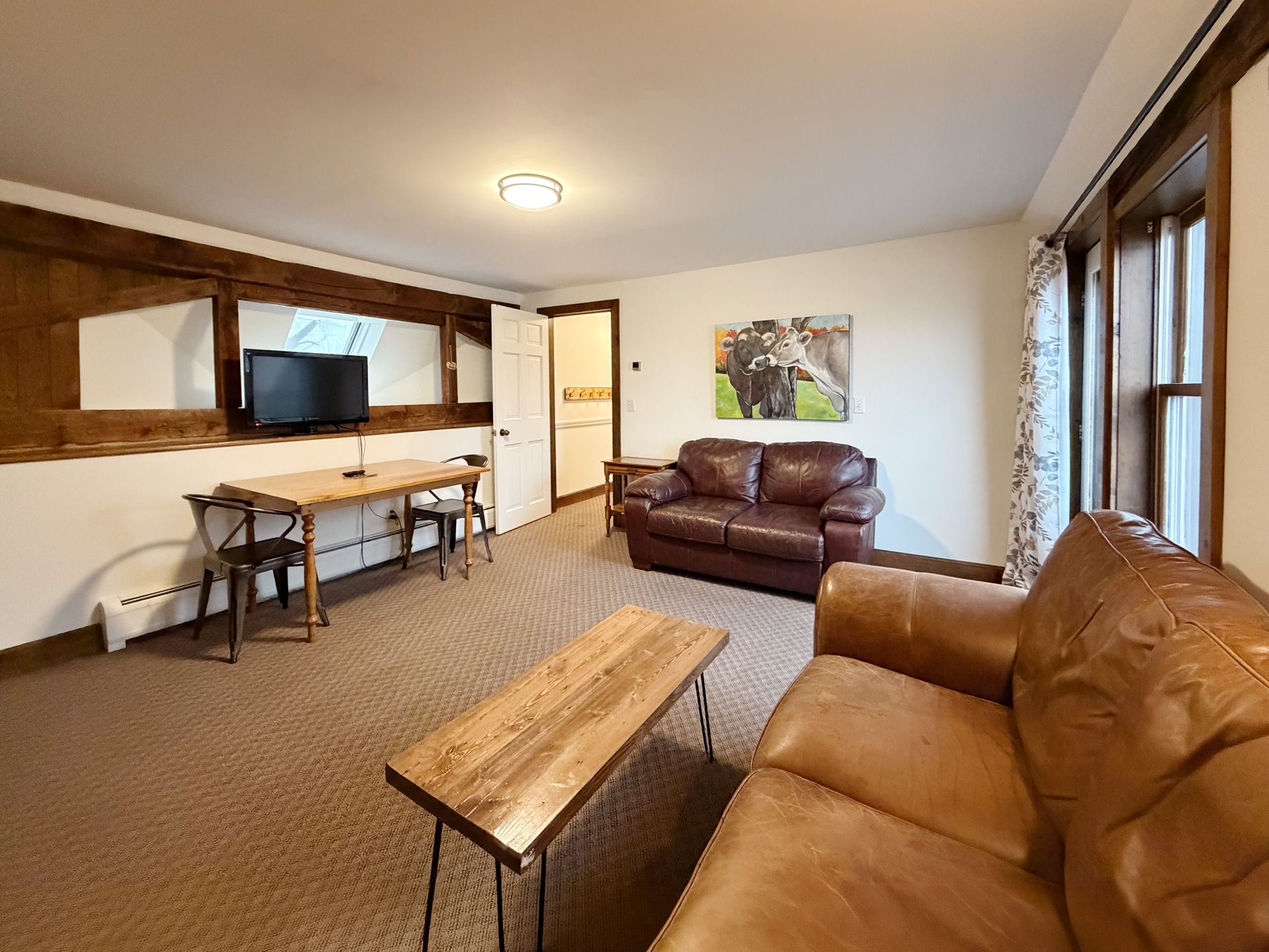 Cozy living room with leather sofas, coffee table, TV, and large windows with wood trim.