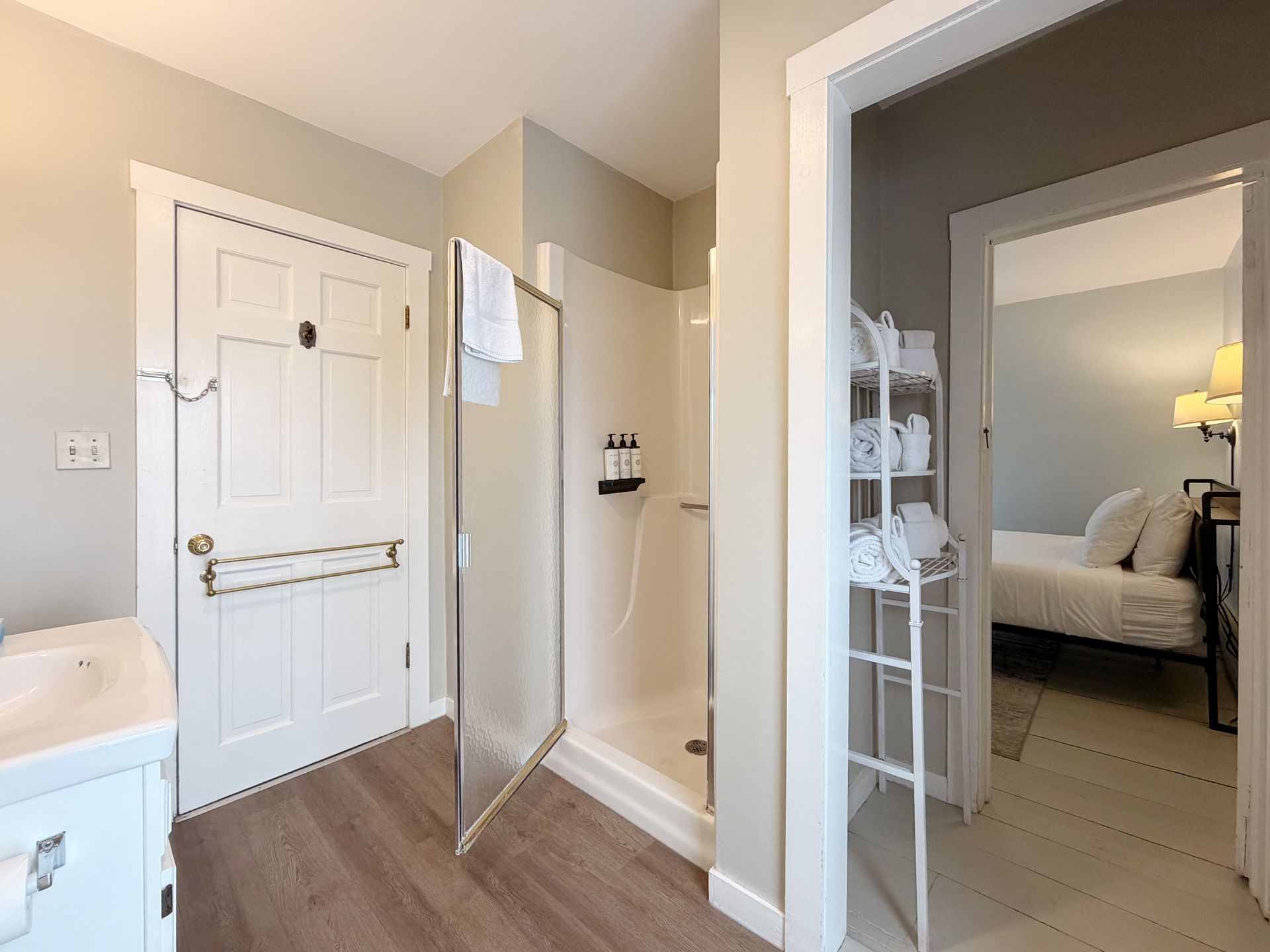 Hallway with open bathroom door, white entry door, and glimpse of a bedroom through another doorway.