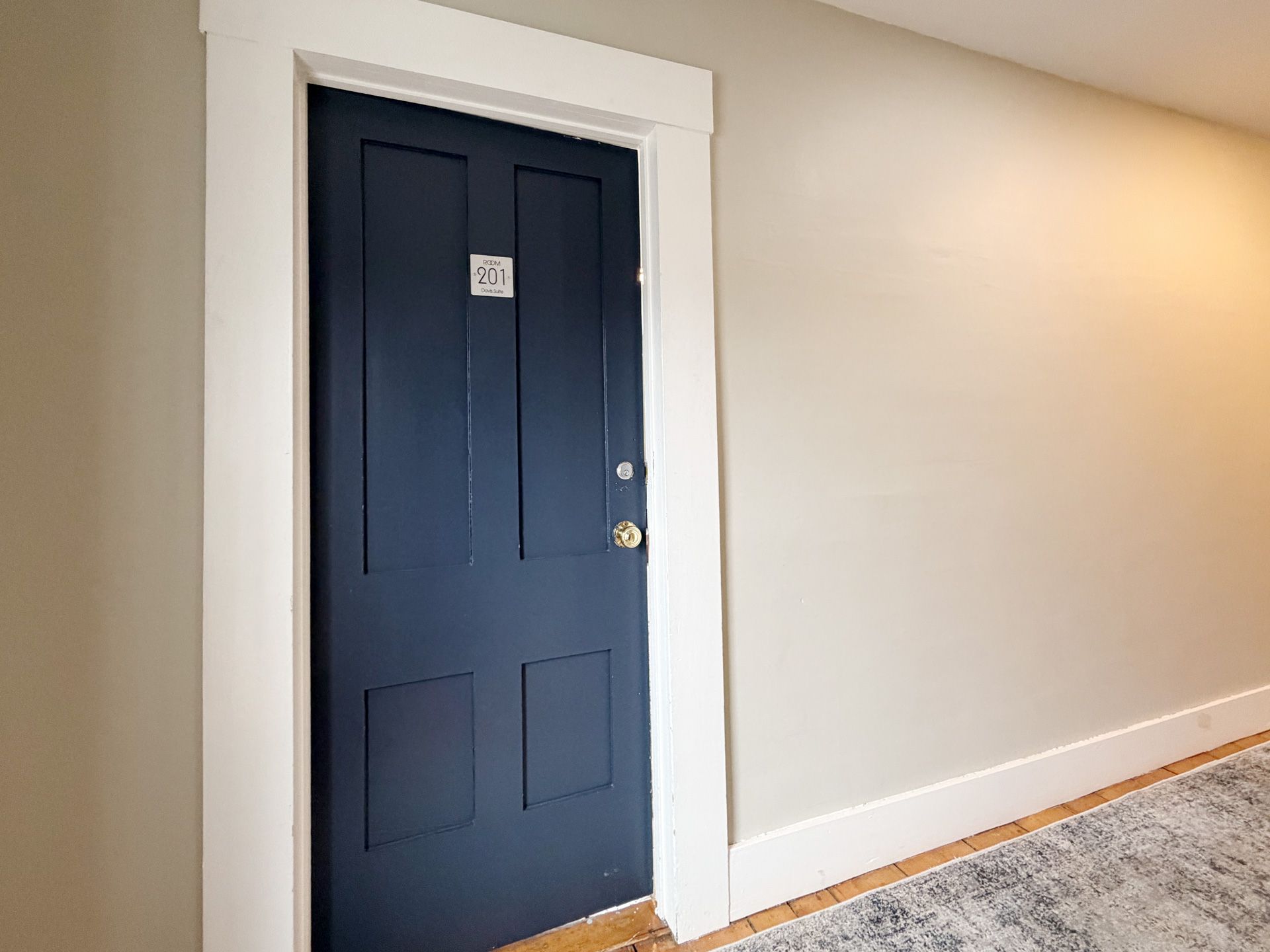 Navy blue front door with white trim in a beige hallway, next to carpet and hardwood flooring.