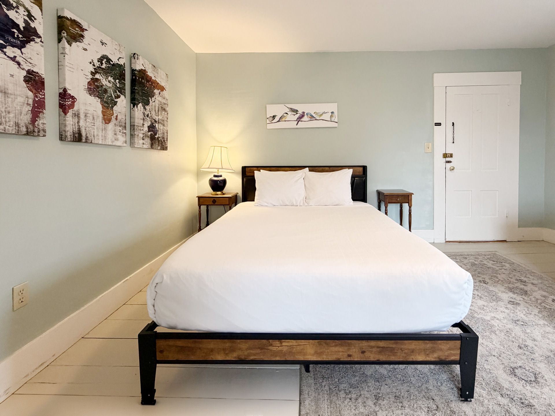 Minimal bedroom with a neatly made bed, nightstands, wall art, and a light-colored rug.