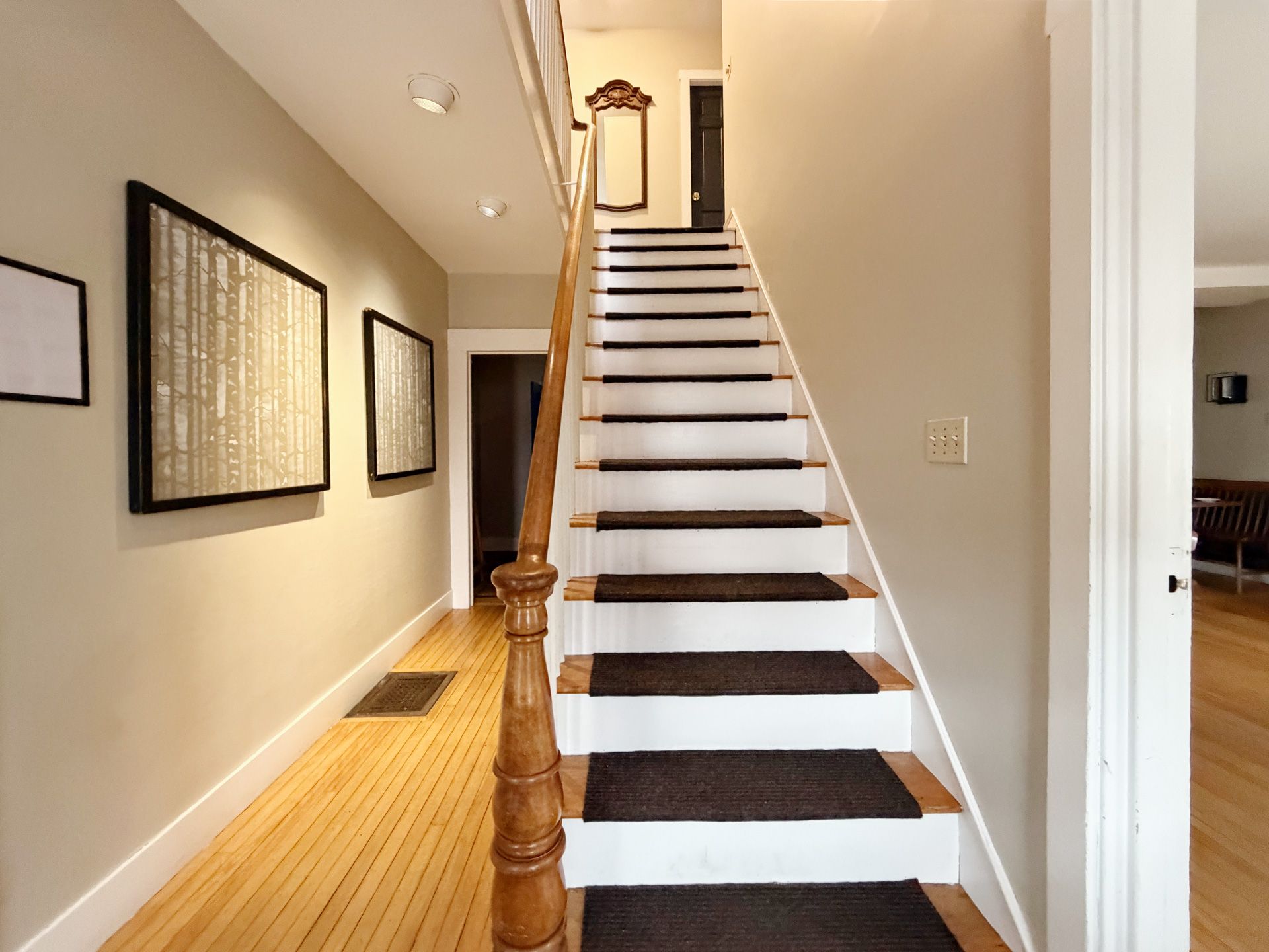 Narrow staircase with dark carpet runners in a bright hallway, viewed from the bottom.