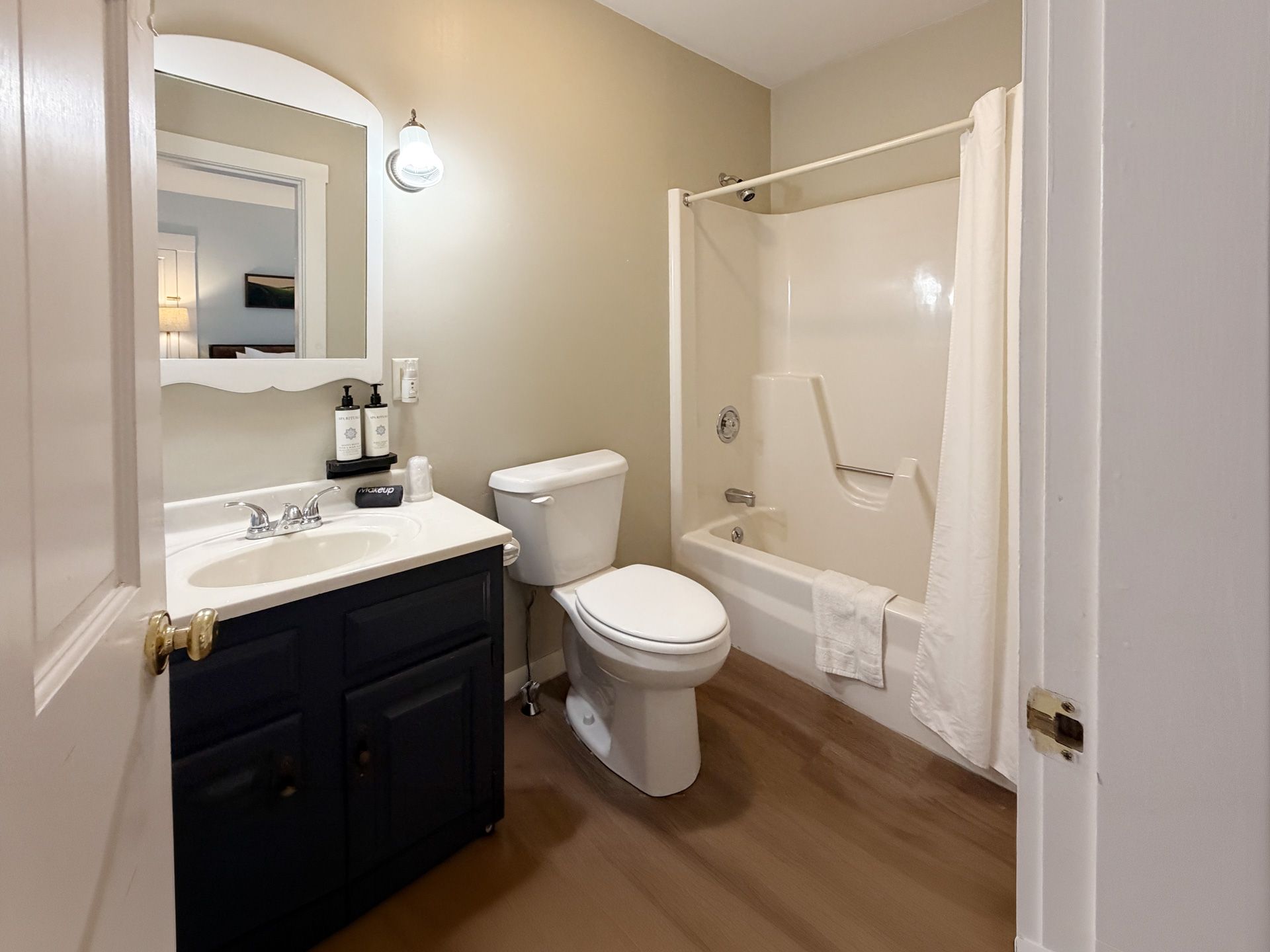 Small beige bathroom with vanity, toilet, and shower/tub combo with white curtain.