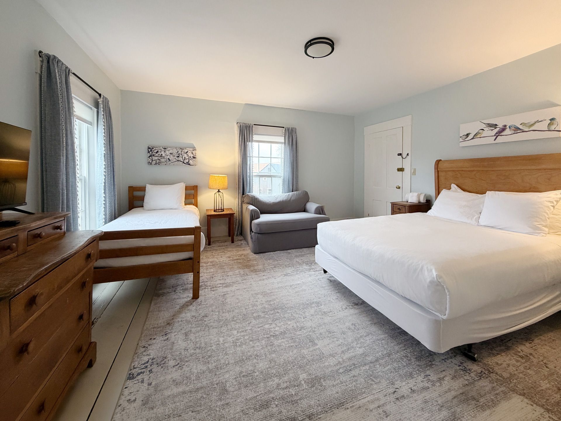 Bright bedroom with two beds, gray chair, dresser, and soft neutral decor