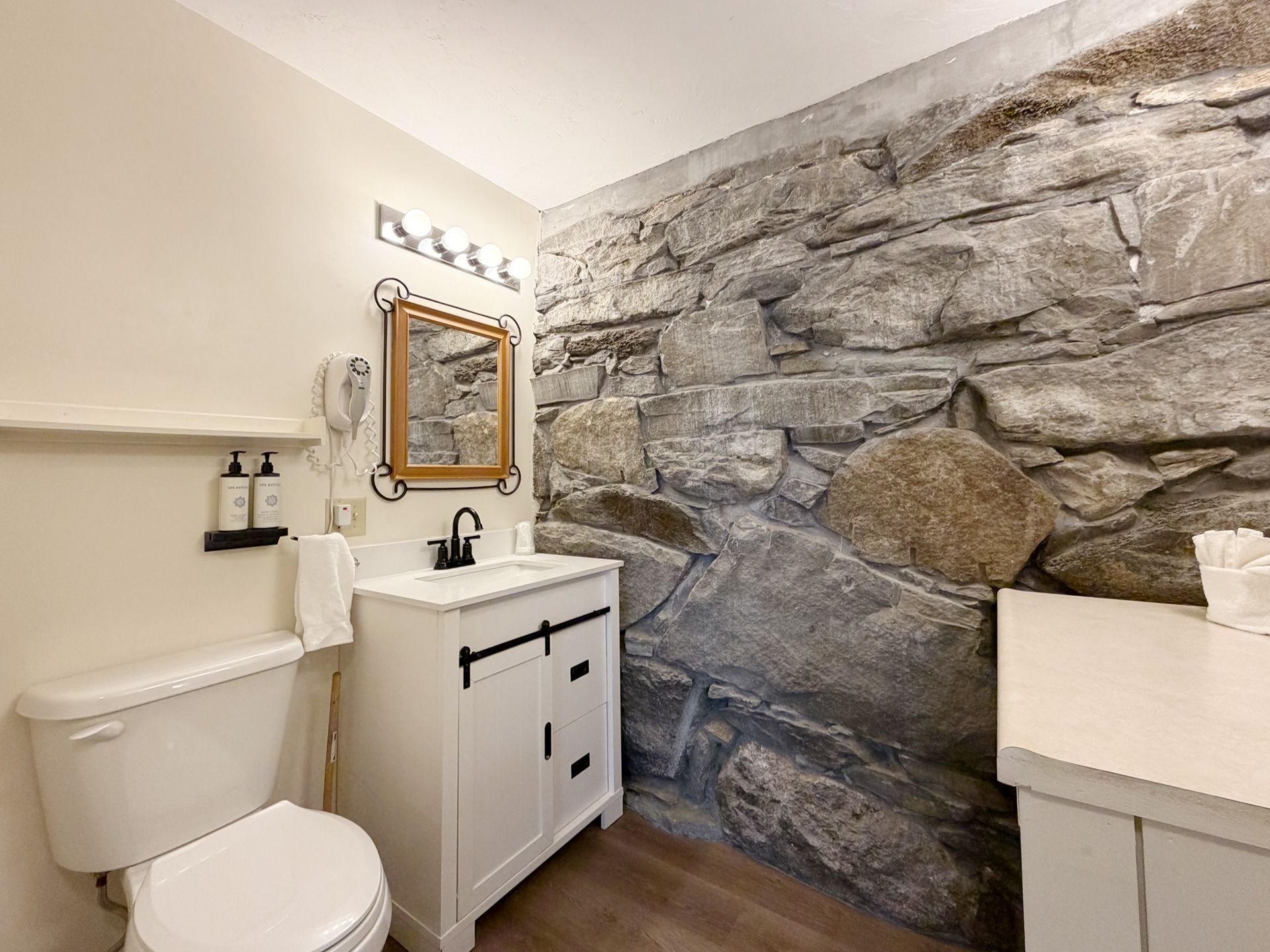 Small bathroom with a toilet, vanity sink, mirror, and stone accent wall