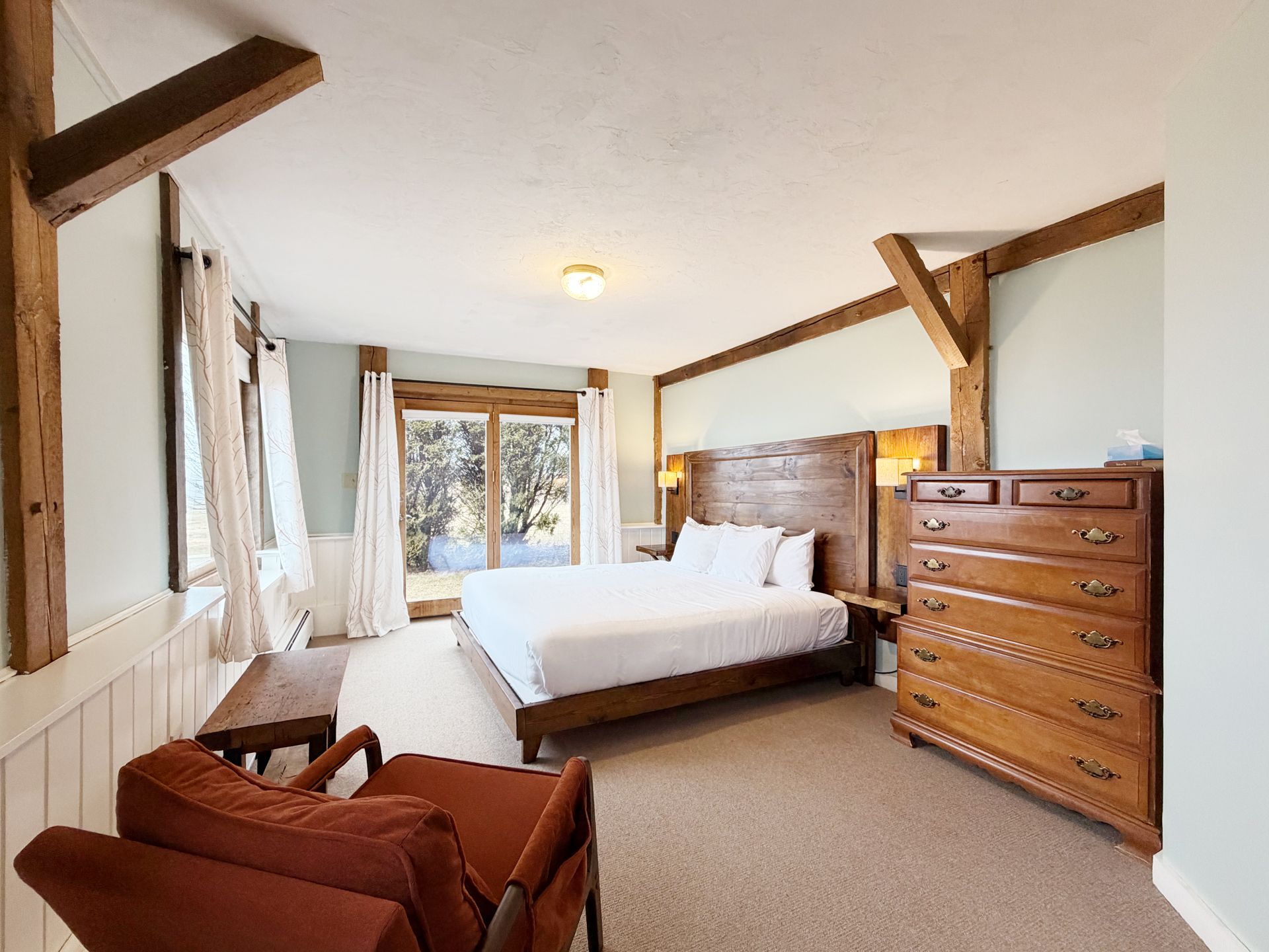 Cozy bedroom with a bed, armchair, dresser, and large windows overlooking snowy trees