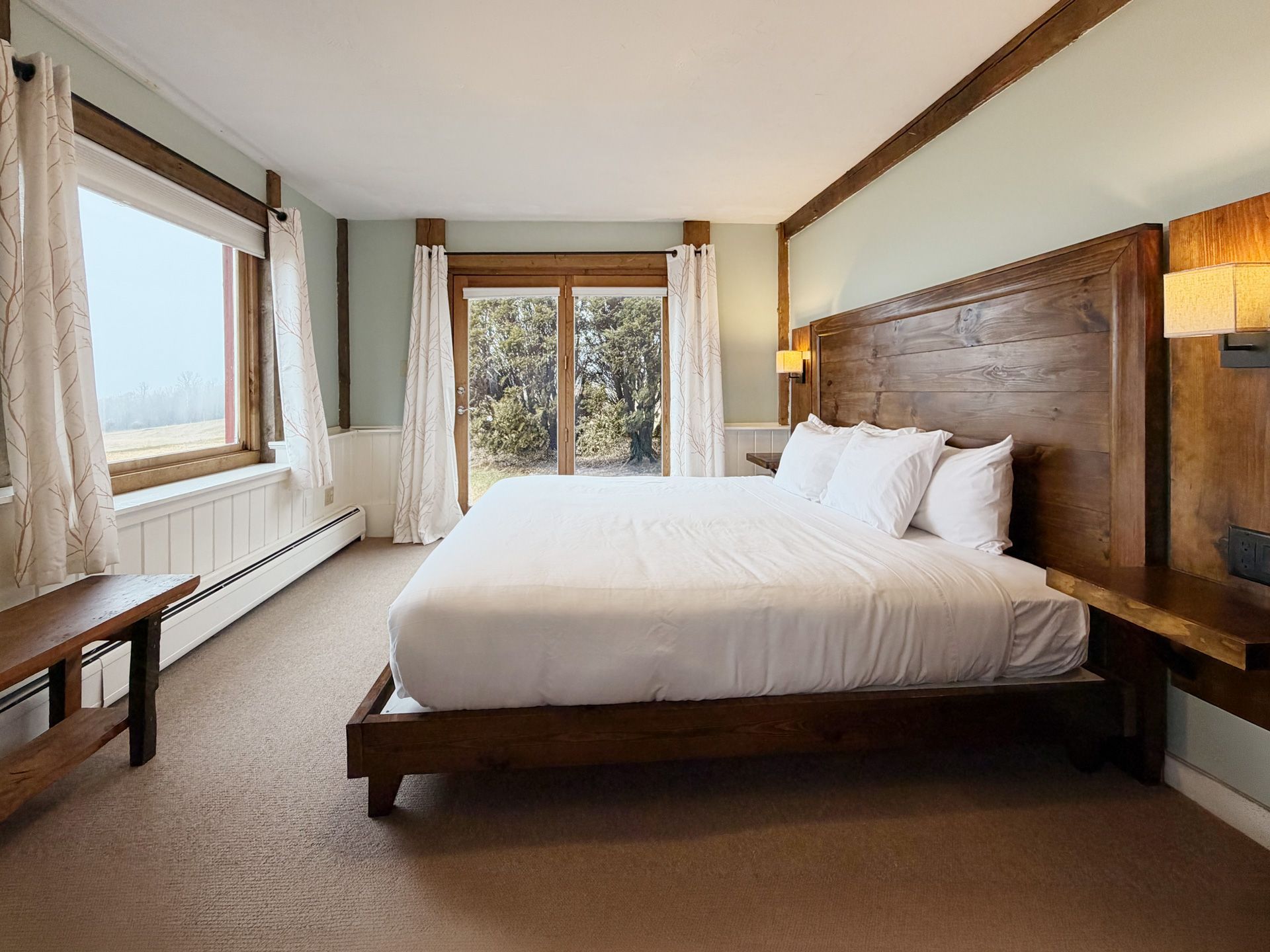 Bright bedroom with a large bed, wood accents, windows, and a sliding glass door to a balcony.