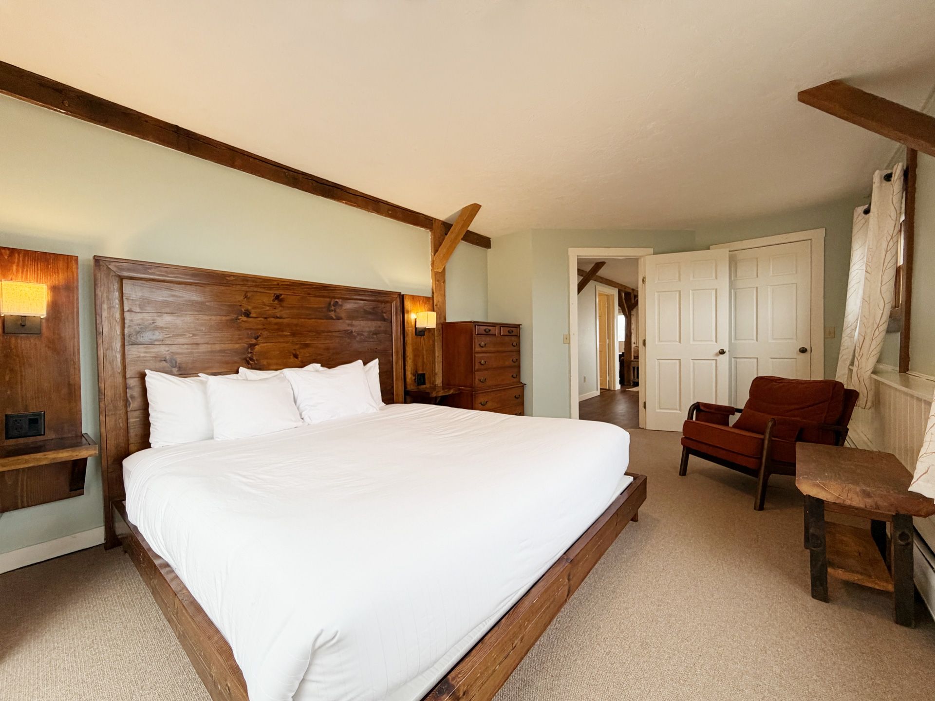 Cozy bedroom with a white bed, wood headboard, armchair, and sloped ceiling