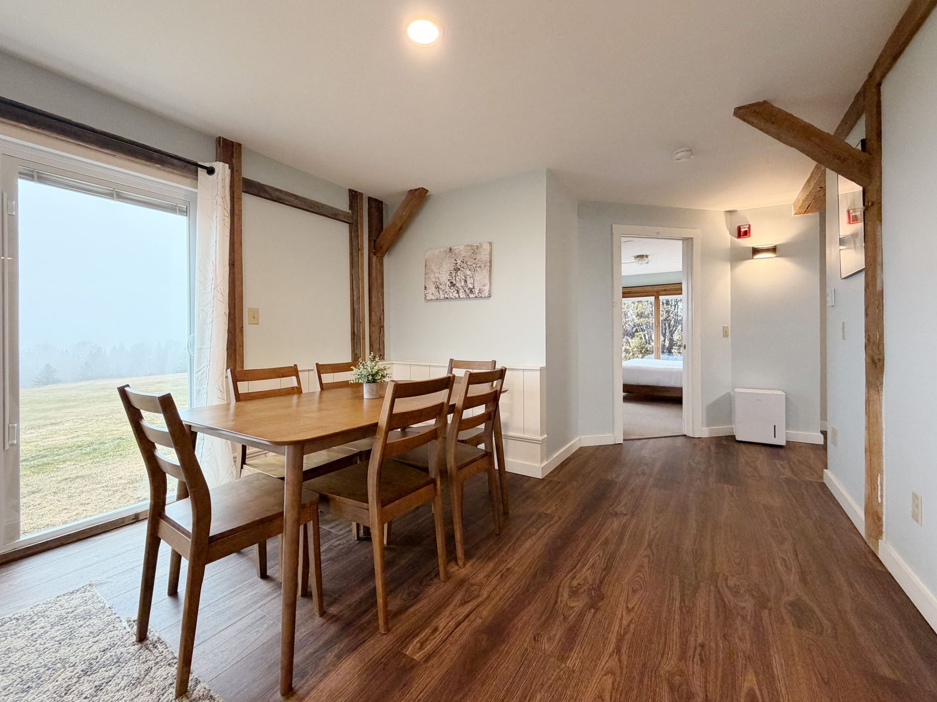 Bright dining room with wooden table, chairs, and large windows overlooking a misty landscape