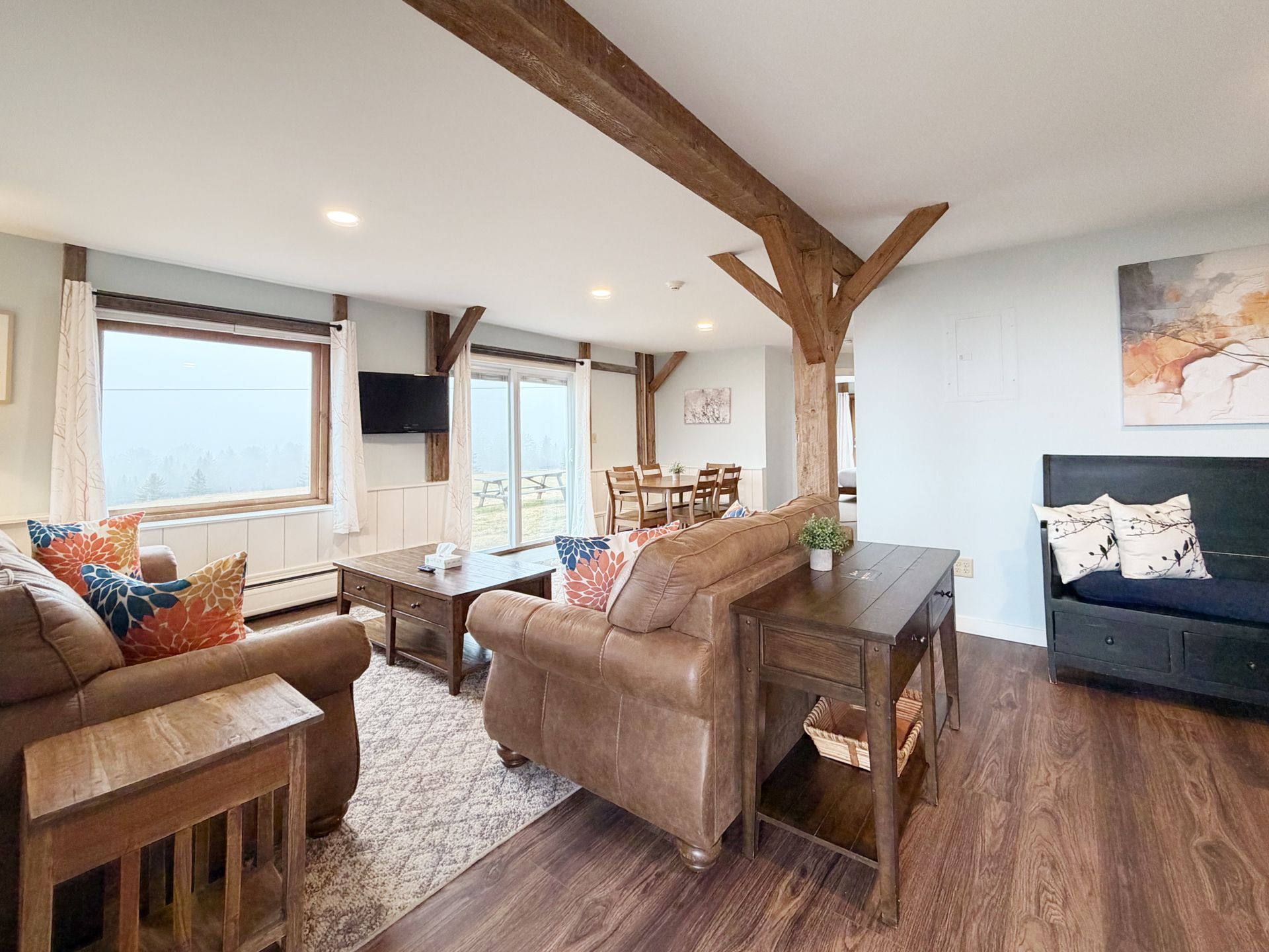 Bright open living room with leather sofas, wood beams, large windows, and a navy loveseat.