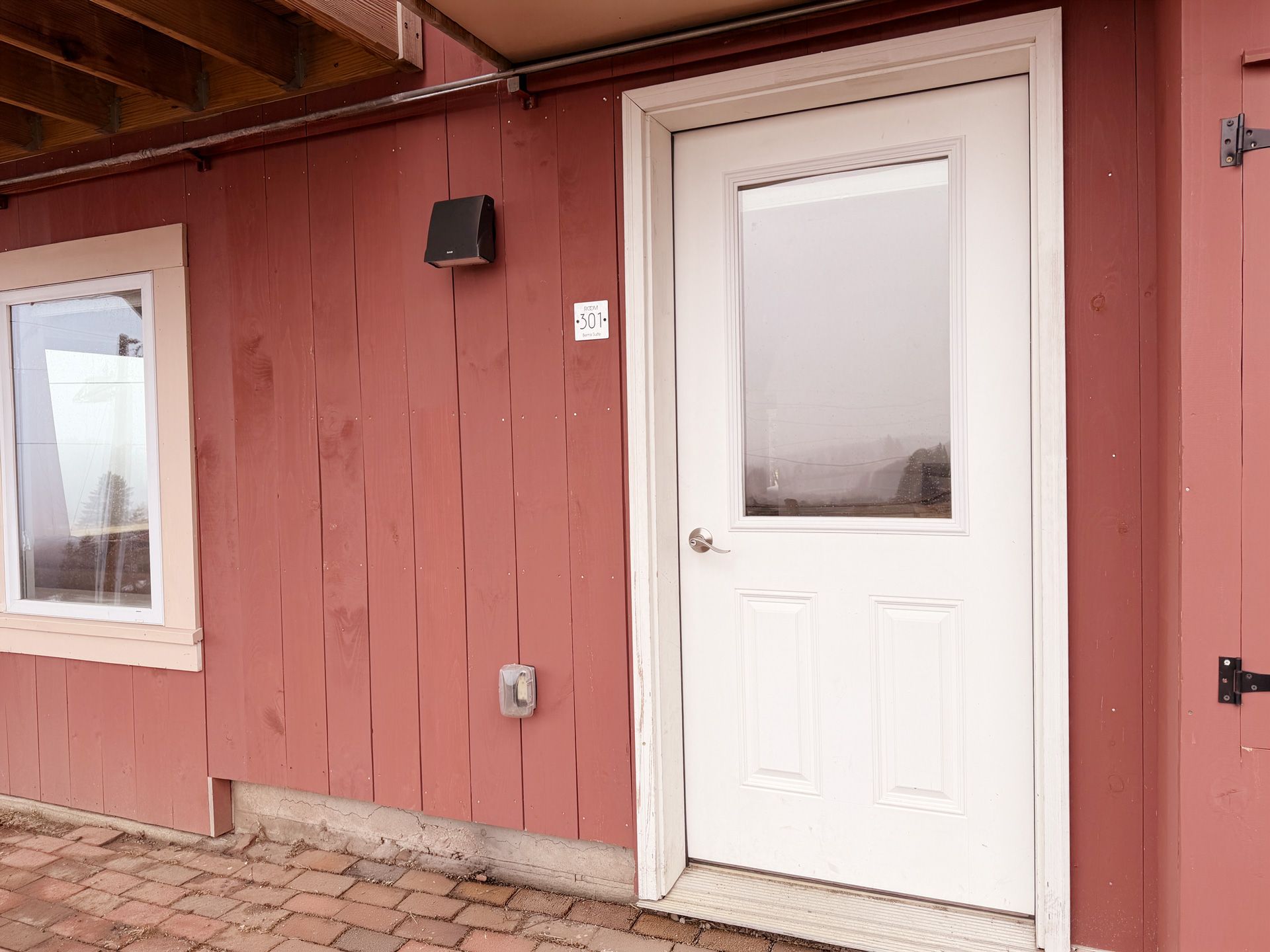 Red building exterior with a white door, window, and brick walkway.