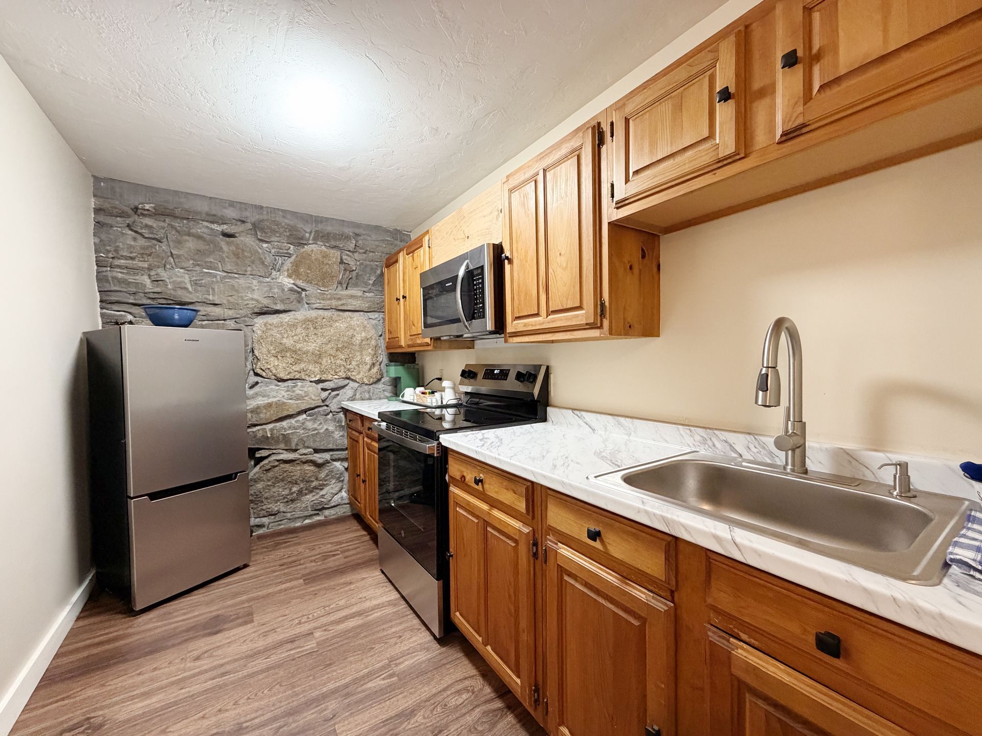 Narrow galley kitchen with wood cabinets, stainless appliances, white counters, and stone accent wall
