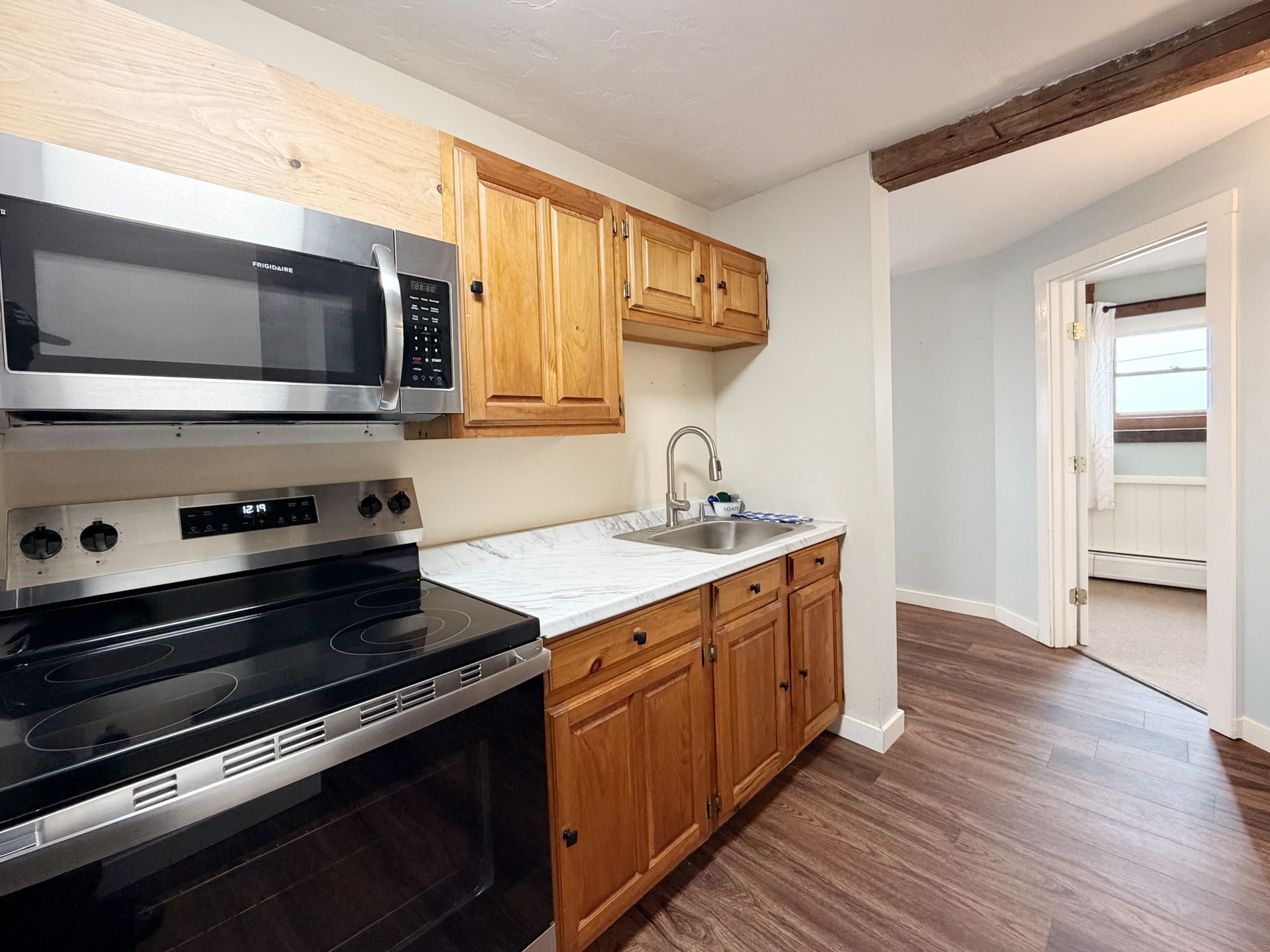 Compact kitchen with stainless steel stove and microwave, wood cabinets, white sink, and wood-look flooring