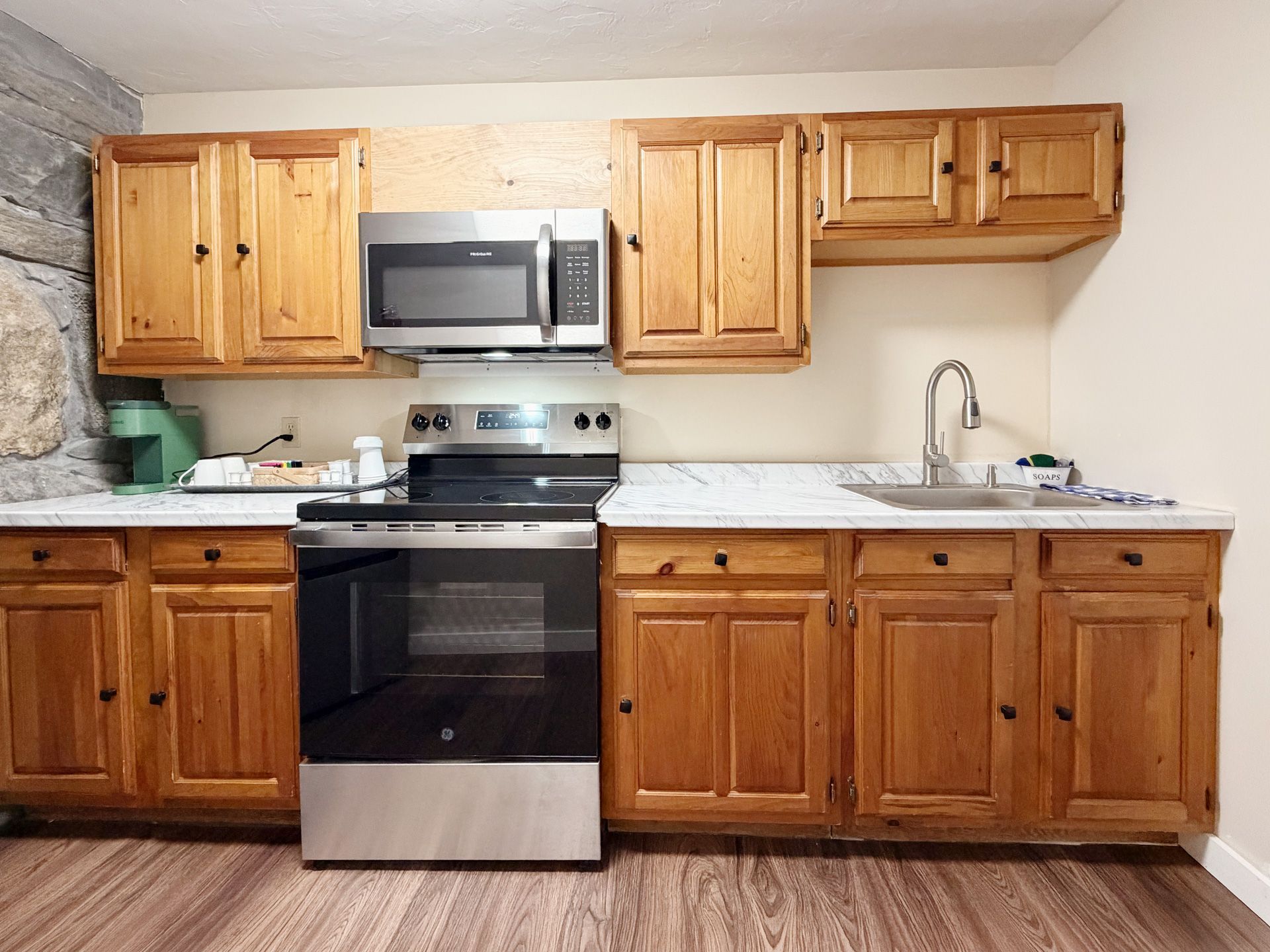 Small kitchen with wood cabinets, black appliances, white countertops, and a sink by a window.