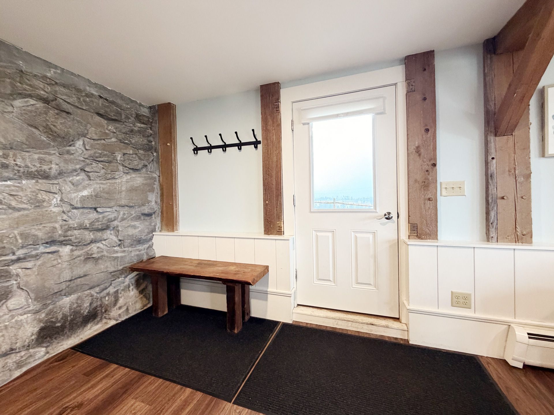 Small mudroom with stone wall, wooden bench, coat hooks, and a white door.