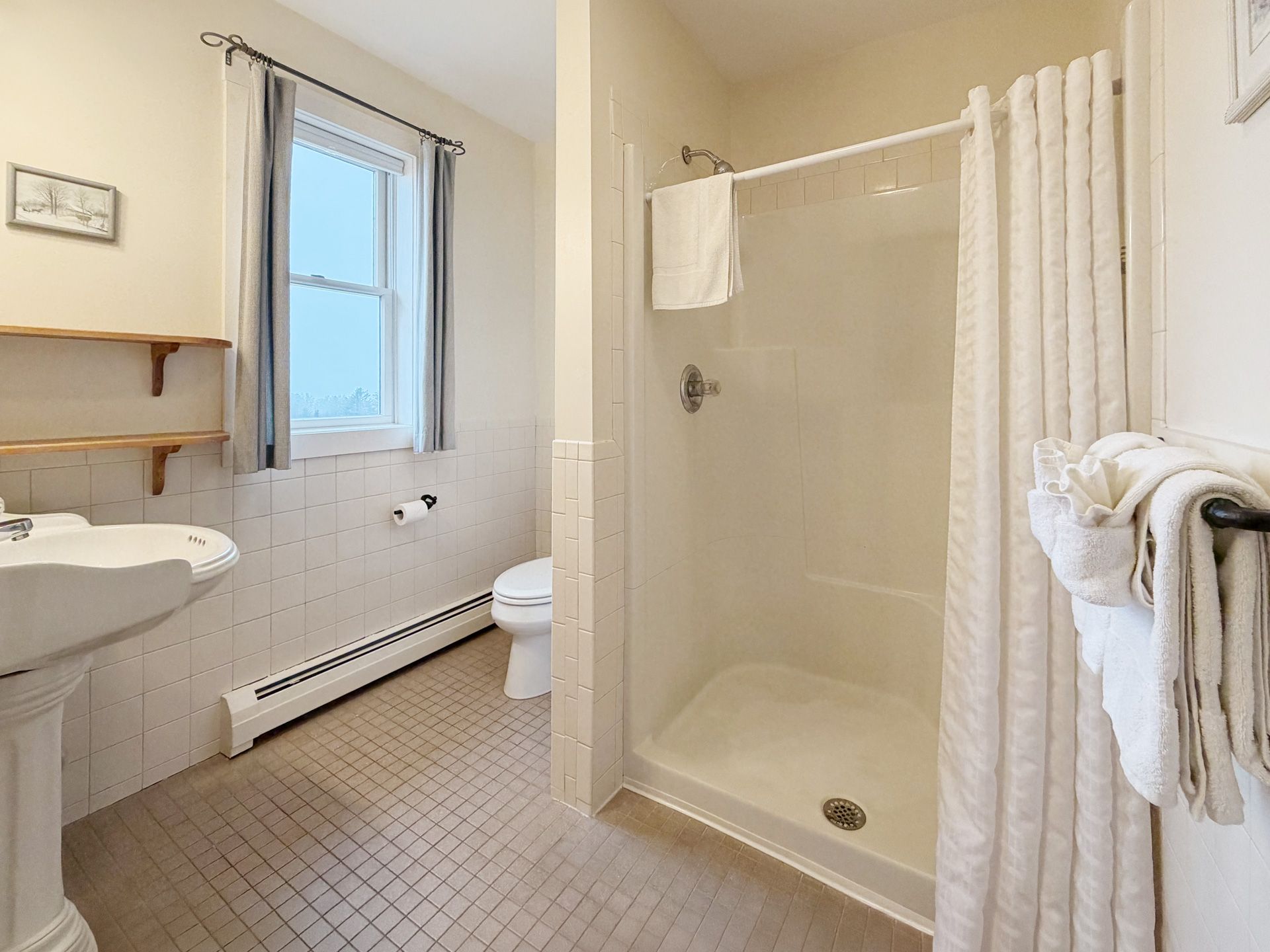 Small bathroom with pedestal sink, window, shower stall, toilet, and towel rack.