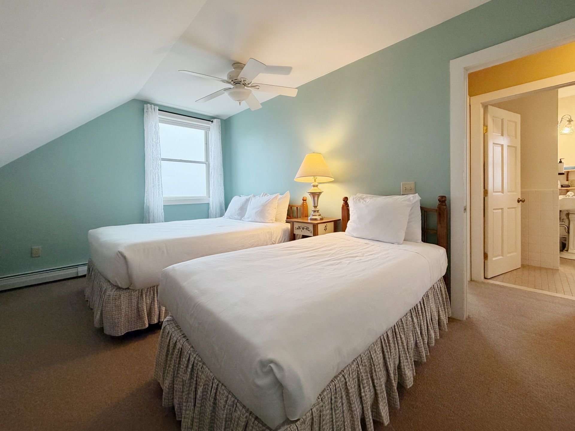 Cozy attic bedroom with two twin beds, pale blue walls, and a lamp by the window