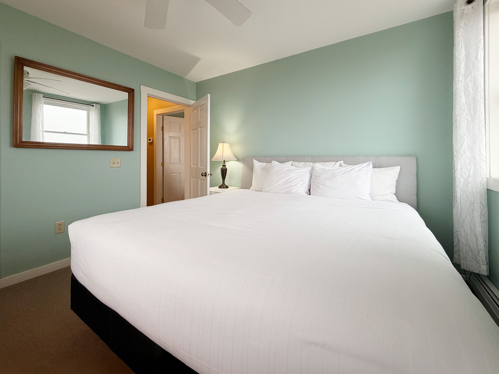 Bright bedroom with a large bed, mint-green walls, mirror, and a bedside lamp.