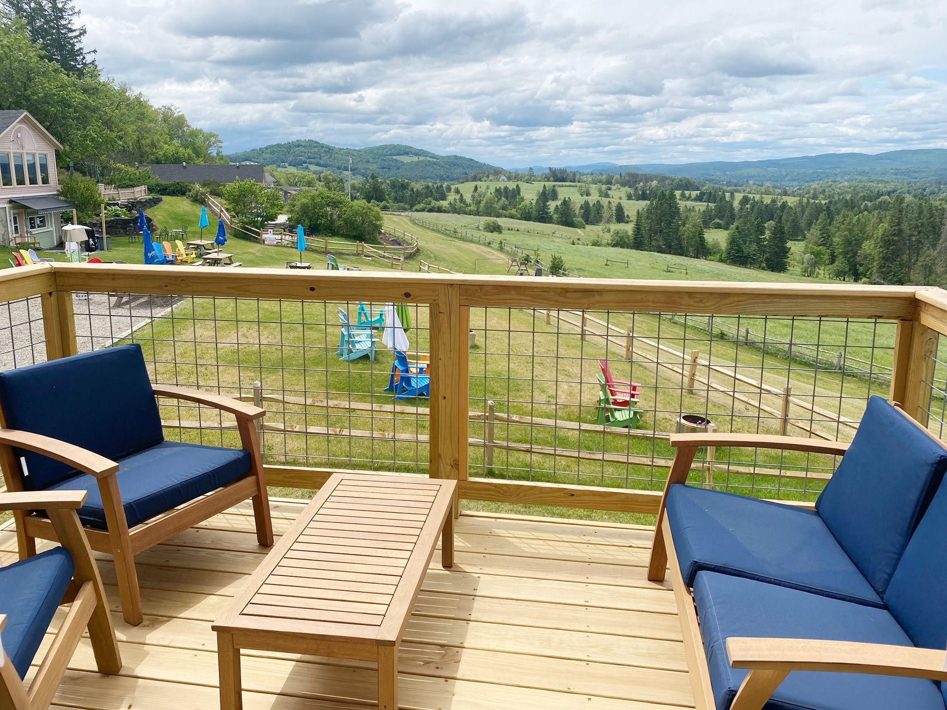 Wooden deck with blue chairs overlooking a green yard, playground, and distant hills under a cloudy sky