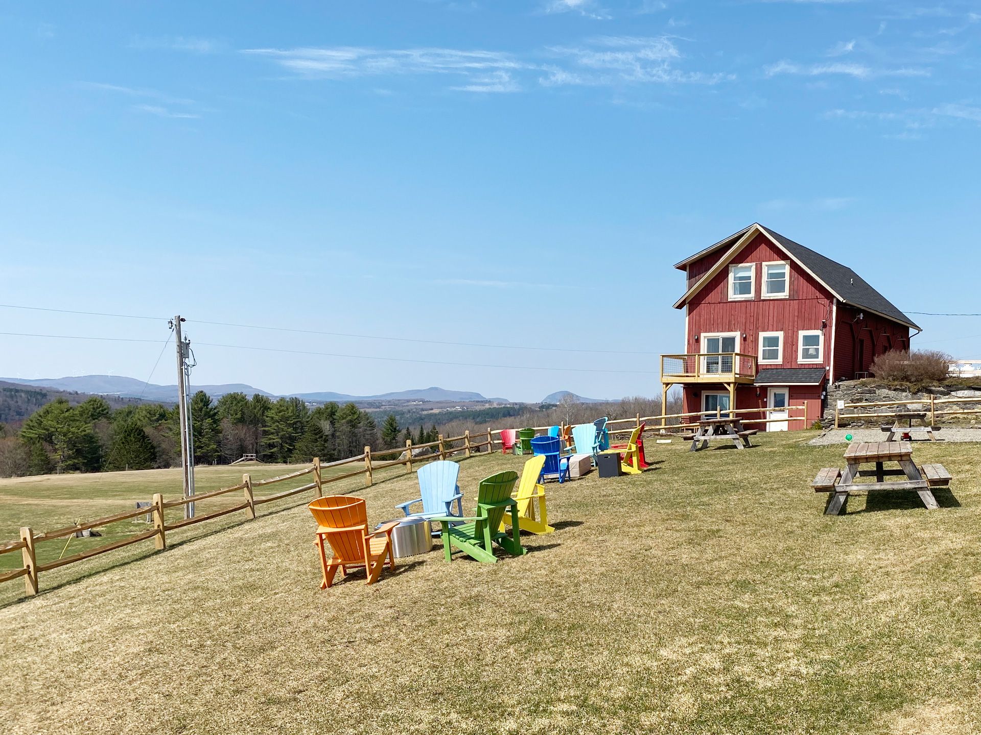 Colorful chairs on a grassy hillside near a red house under a clear blue sky