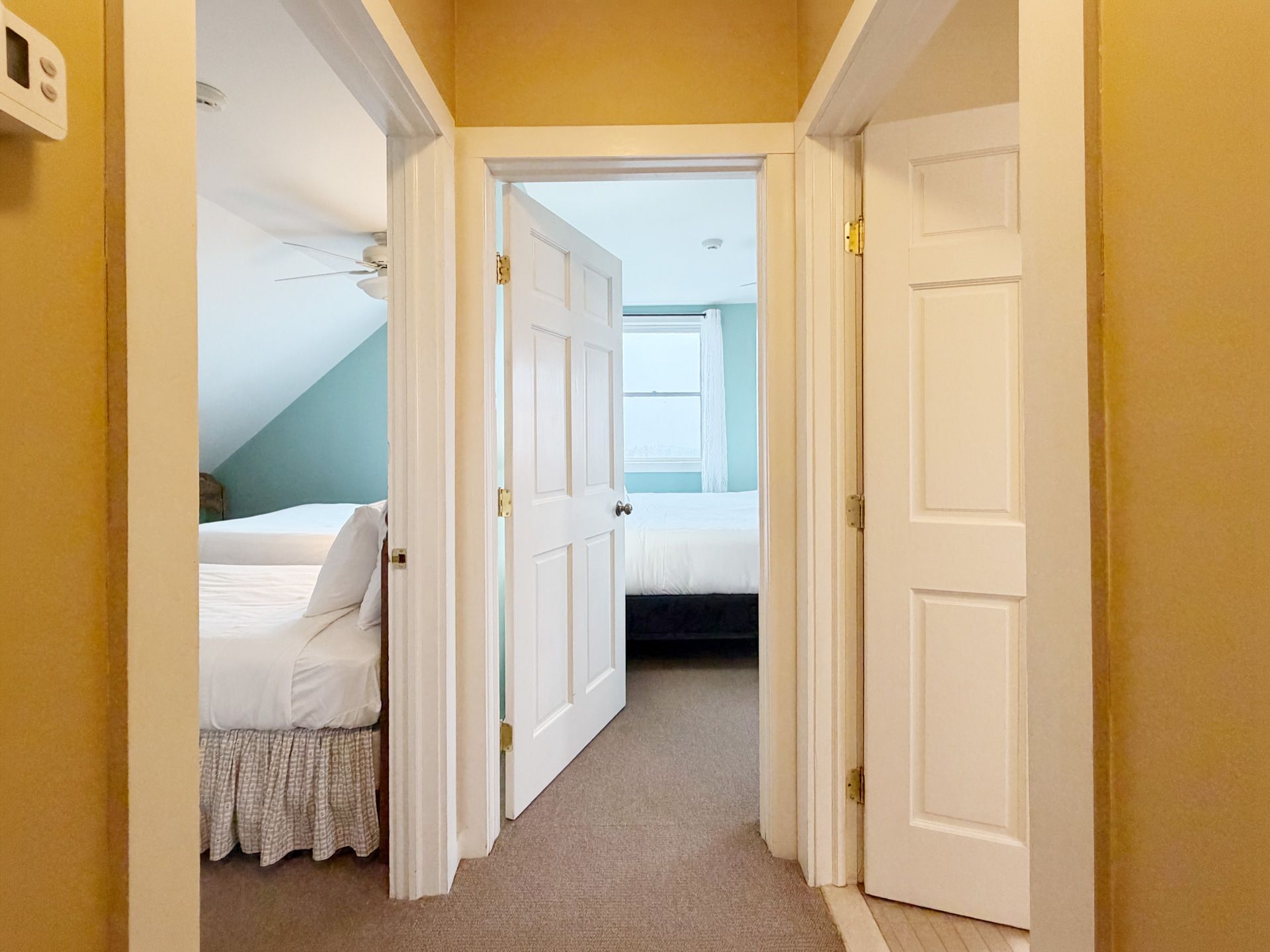 Hallway with three open bedroom doors, beige walls, and carpeted floor in a home