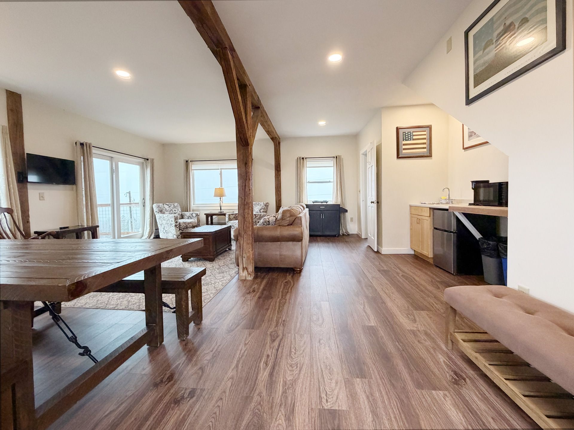 Bright open living-dining room with wood floors, exposed beam, sofa, table, and kitchen area