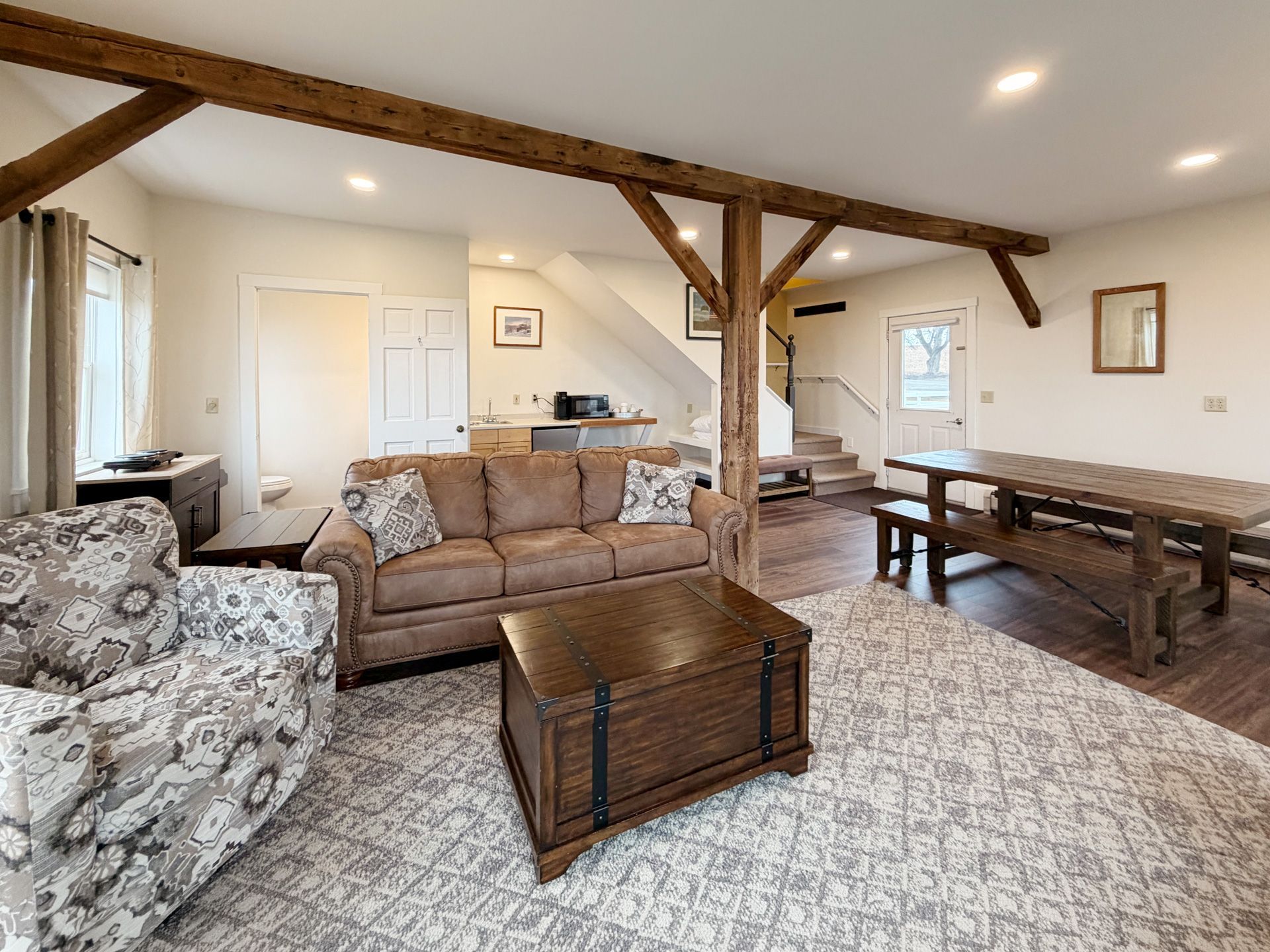 Spacious living room with beige sectional, patterned chairs, wooden coffee table, and exposed beam ceiling