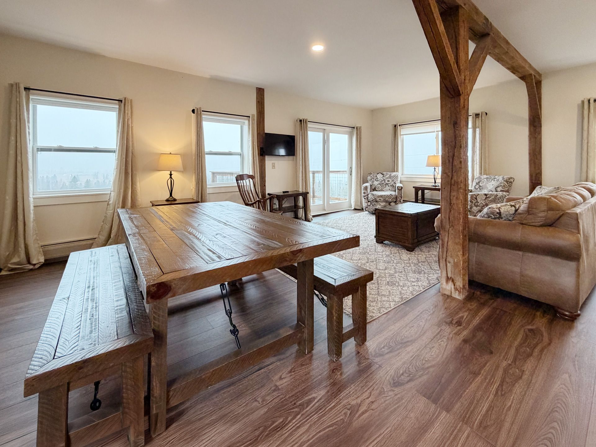 Cozy open-plan living room with wooden dining table, sofa, chairs, and large windows