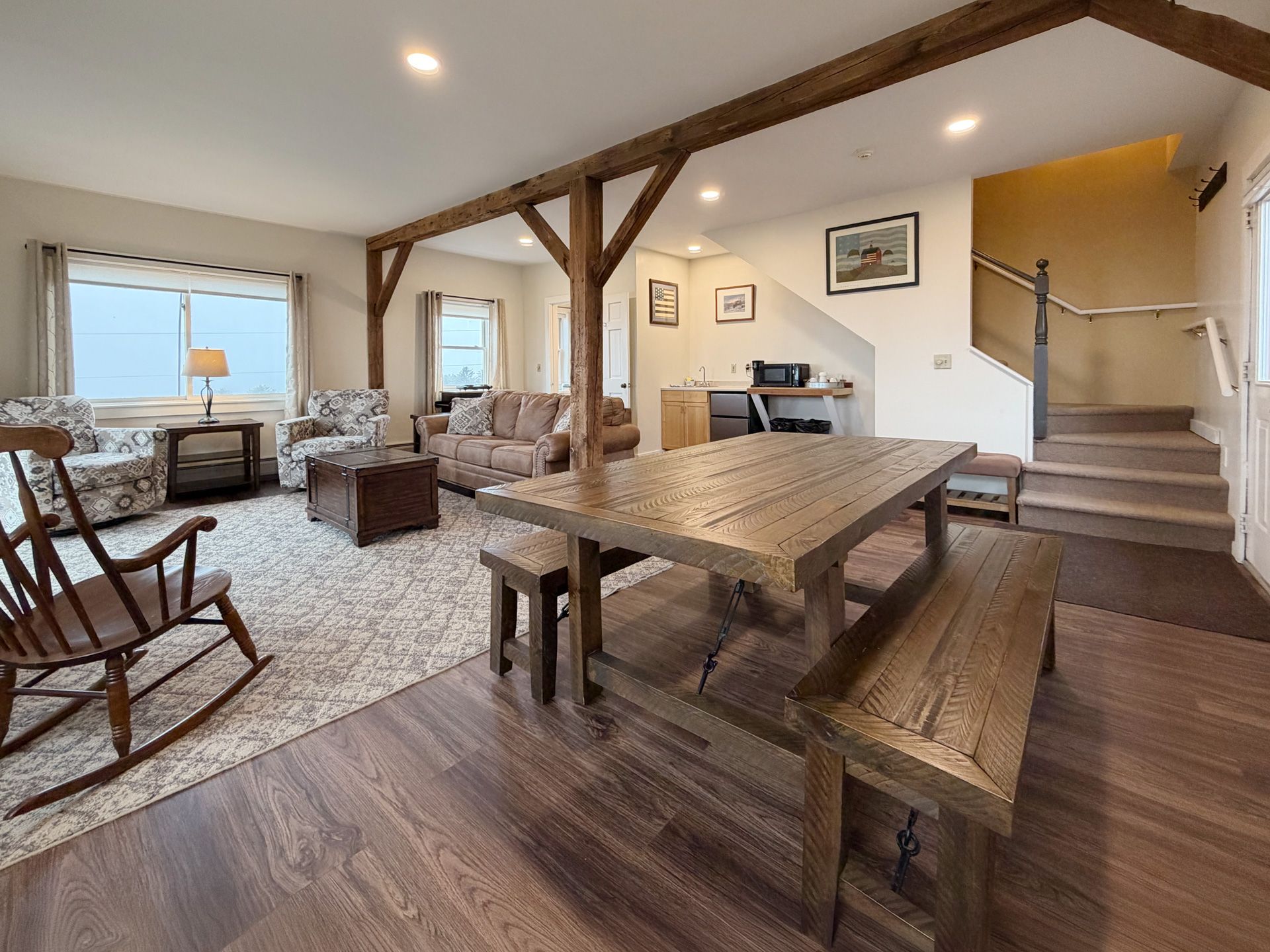 Open-concept dining and living room with wood beams, fireplace, and large windows