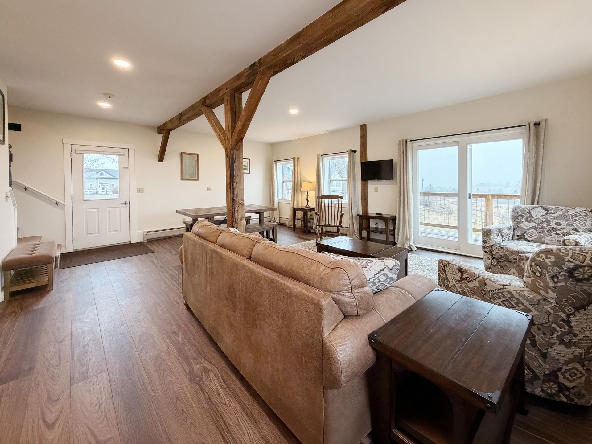 Spacious living room with exposed wooden beams, beige sofa, patterned armchairs, and large windows.