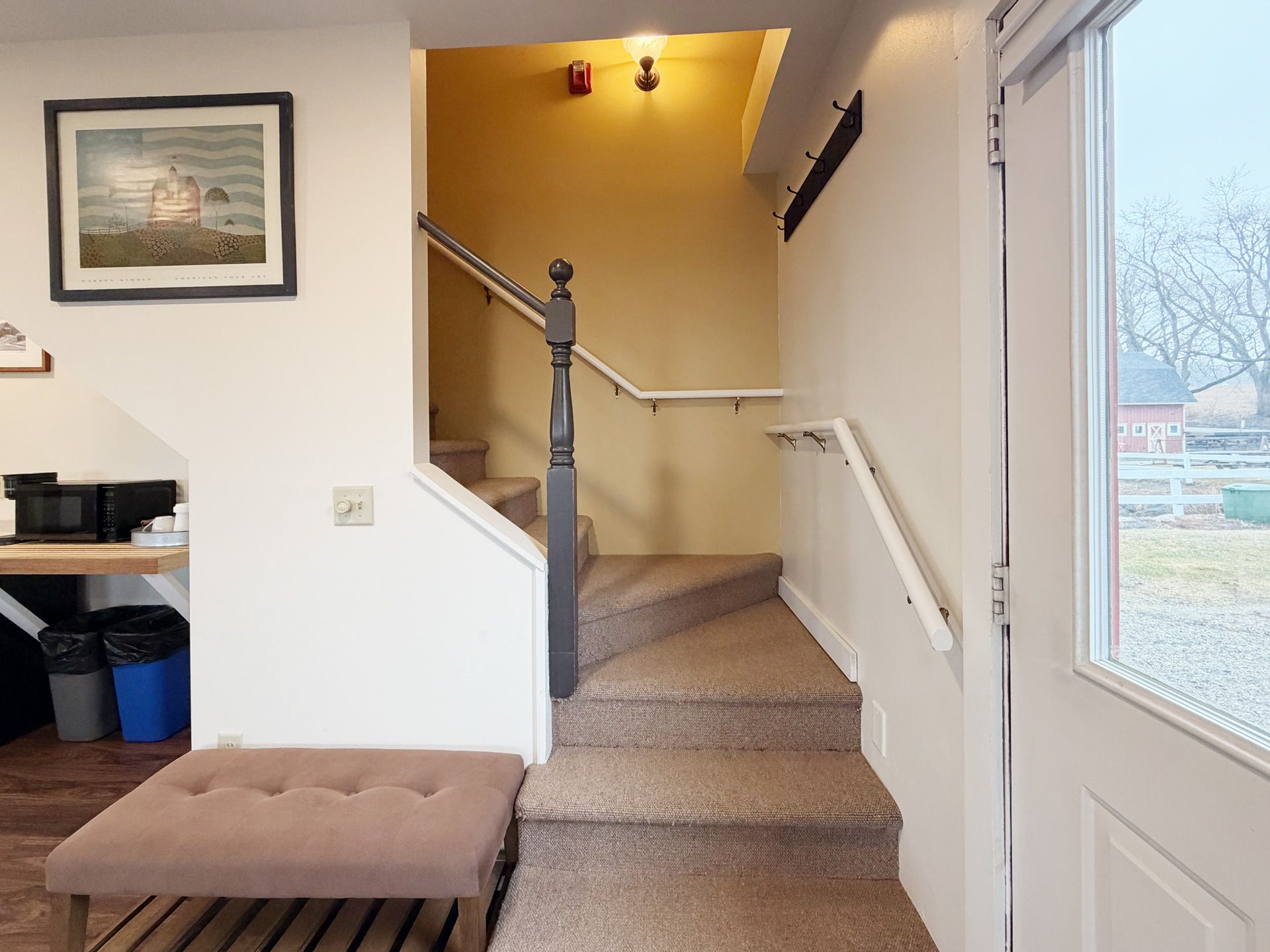 Entryway with carpeted stairs, white walls, and a front door beside a small bench.