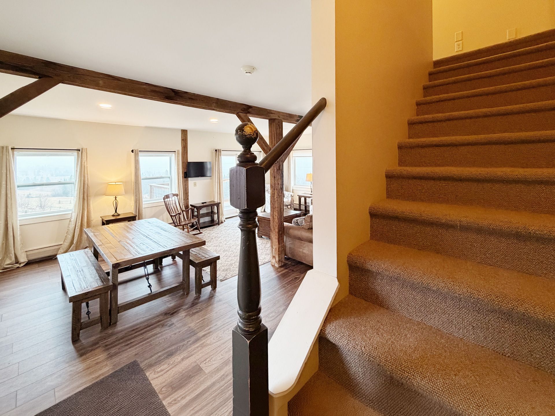 Staircase beside a bright dining room with wooden beams and a long table