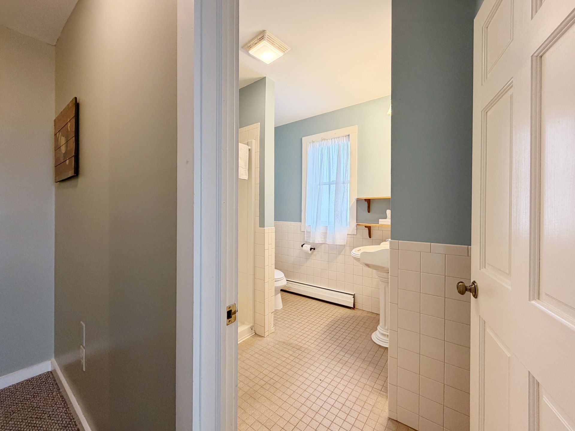 Bright hallway opening into a bedroom with white doors, beige carpet, and blue-gray walls.