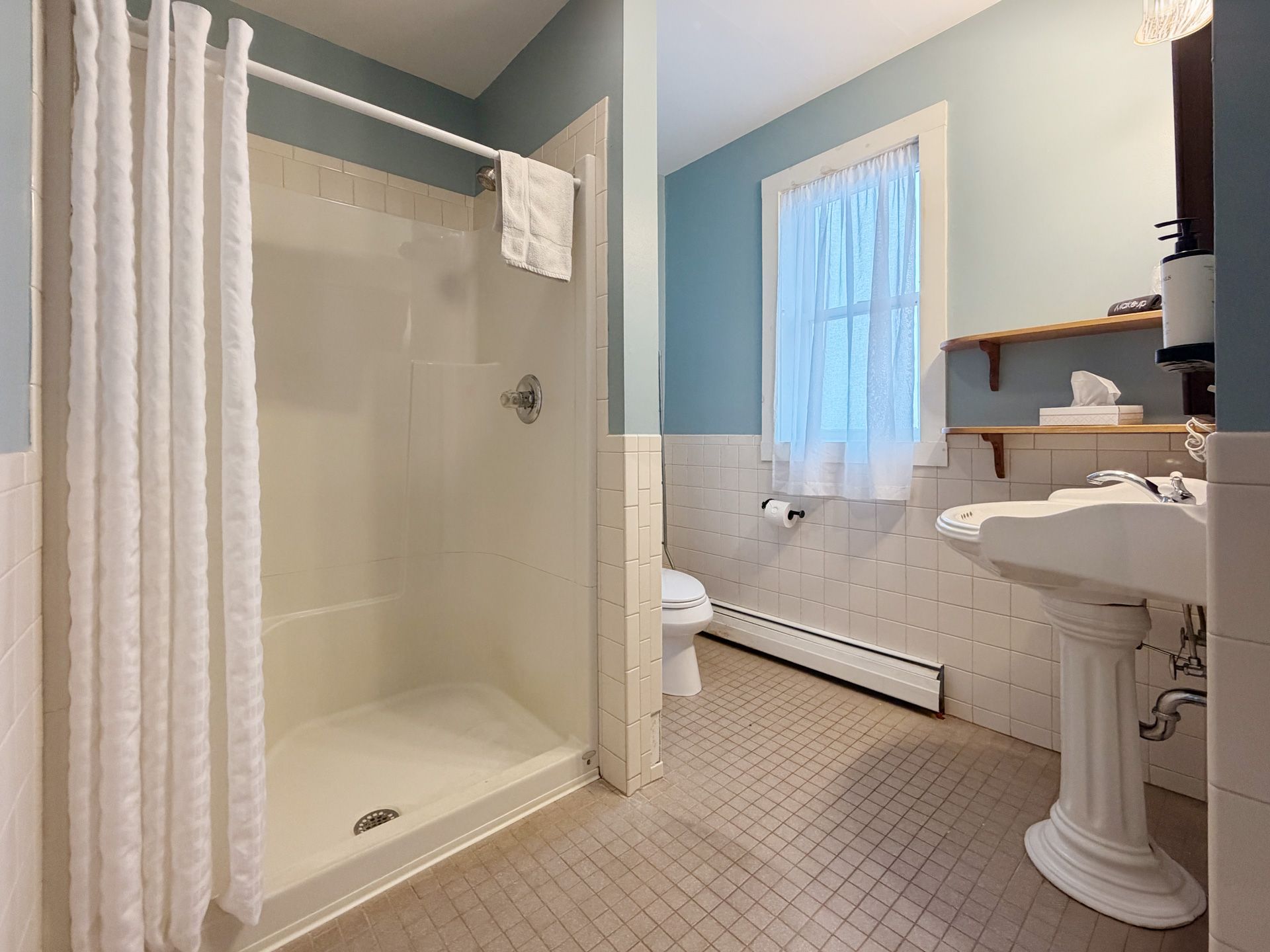 Accessible bathroom with walk-in shower, pedestal sink, toilet, and light blue walls