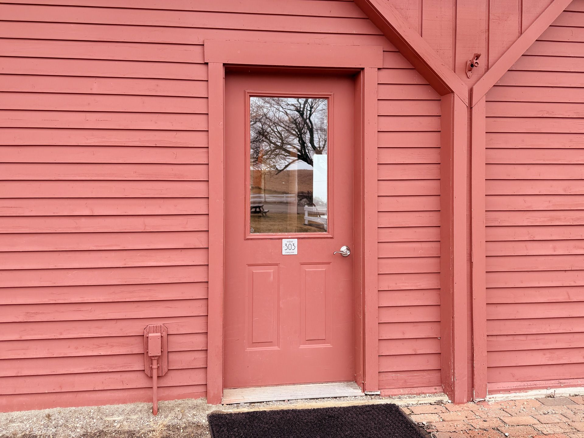 Coral door set in matching red wooden siding, with a small window and stone step.