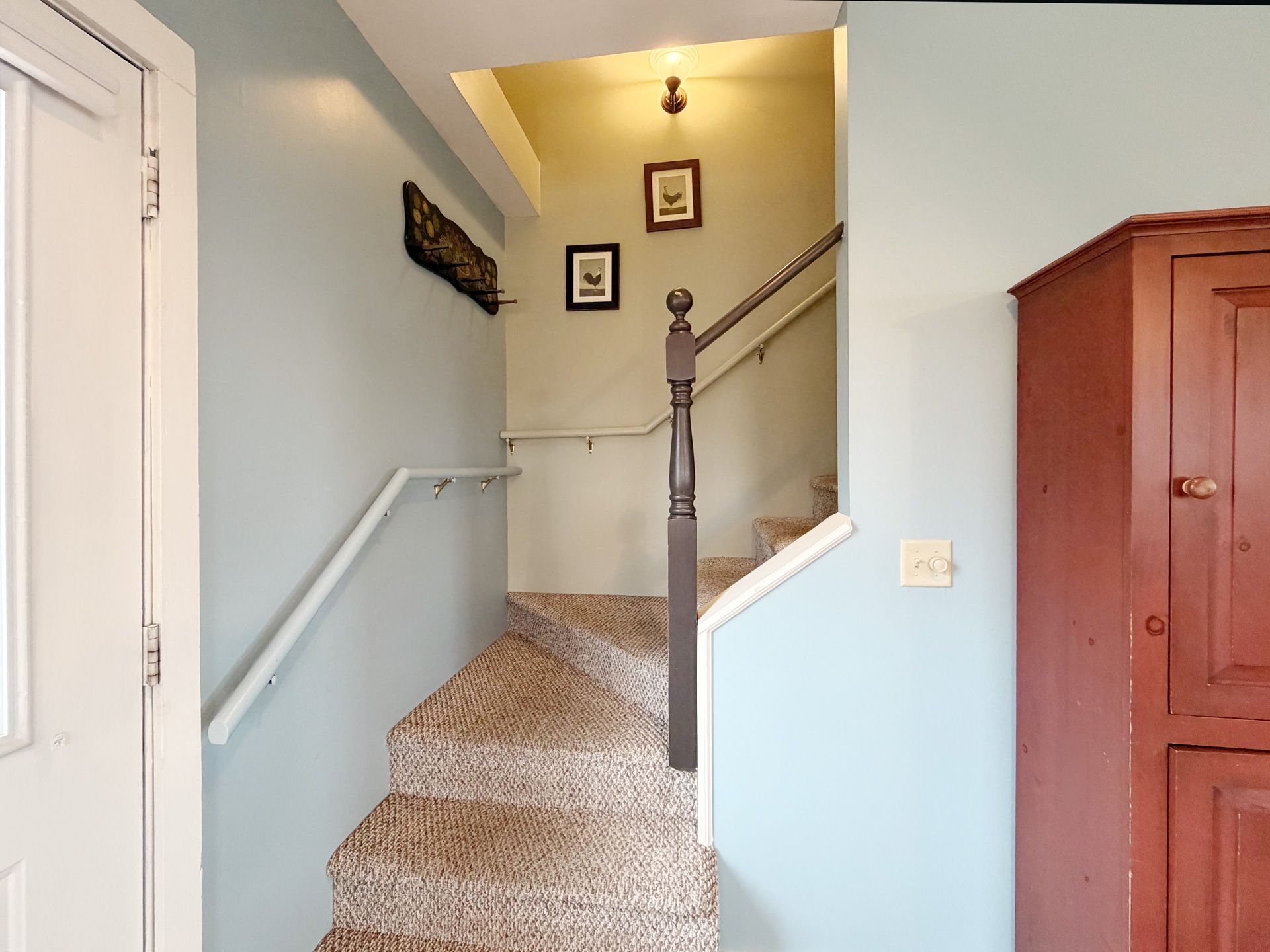 Carpeted staircase with white walls, light blue hall, and red cabinet at the top landing